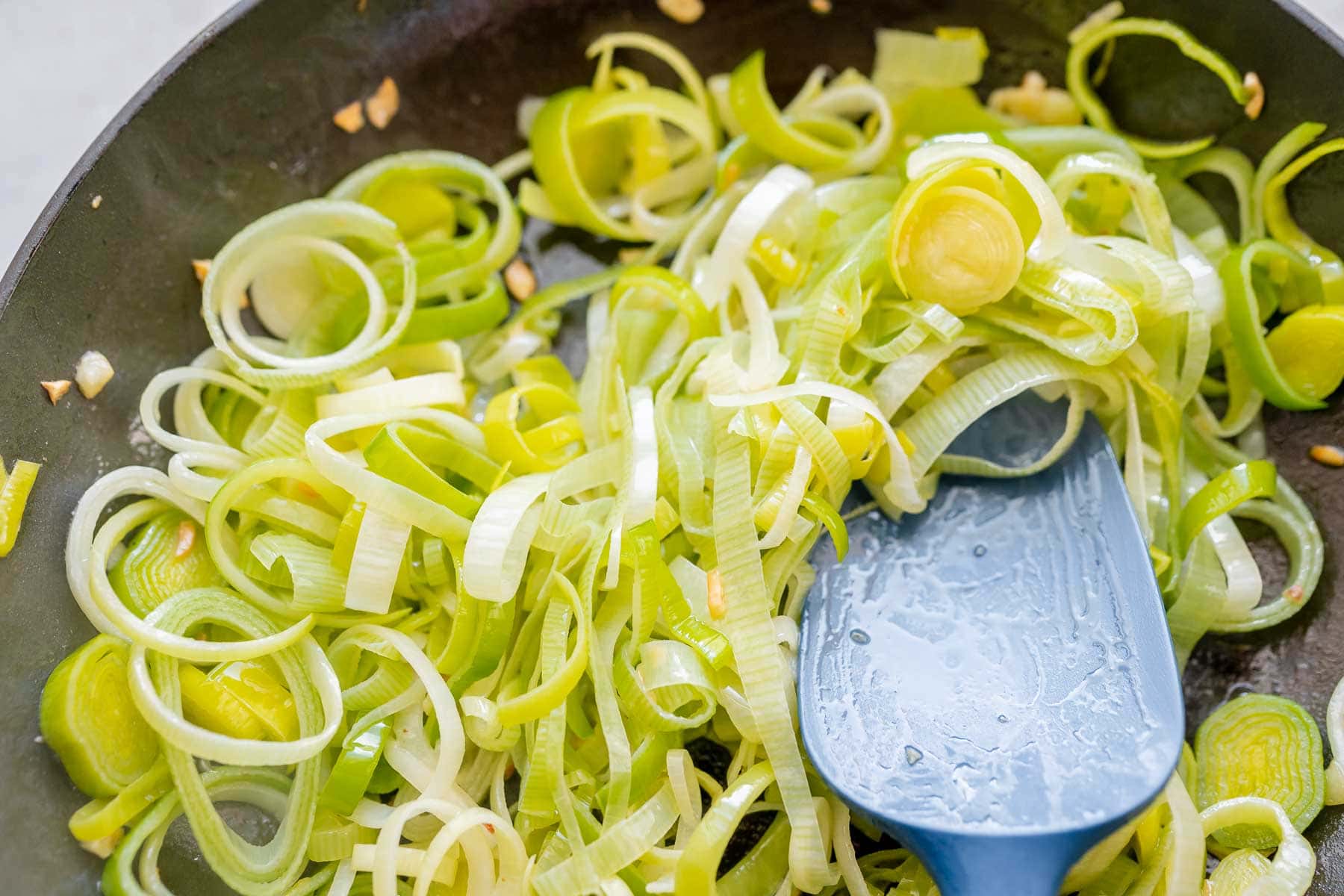 A blue spatula rests in a skillet of sliced leeks.