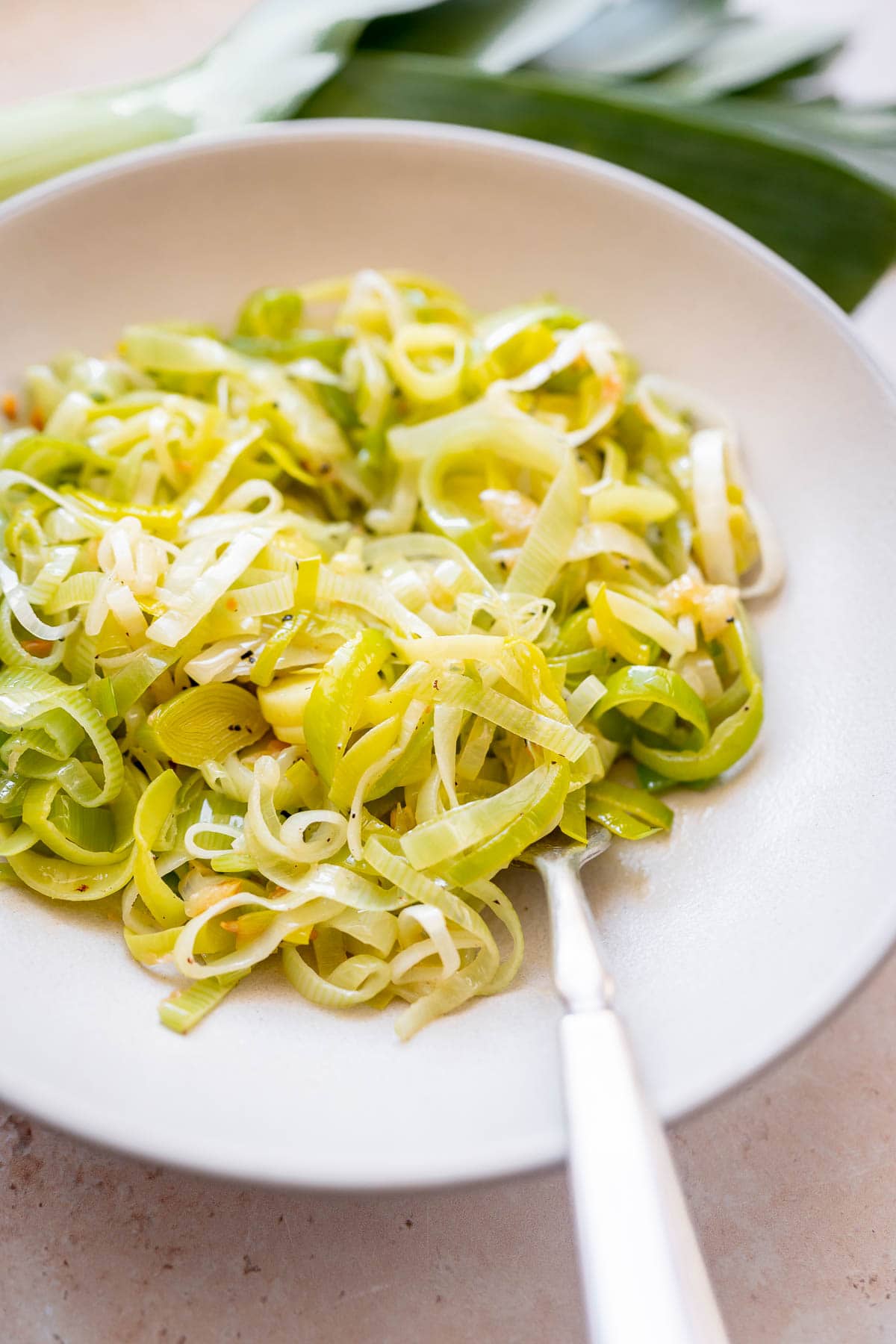 A silver fork rests in a ceramic bowl of hot buttered leeks.