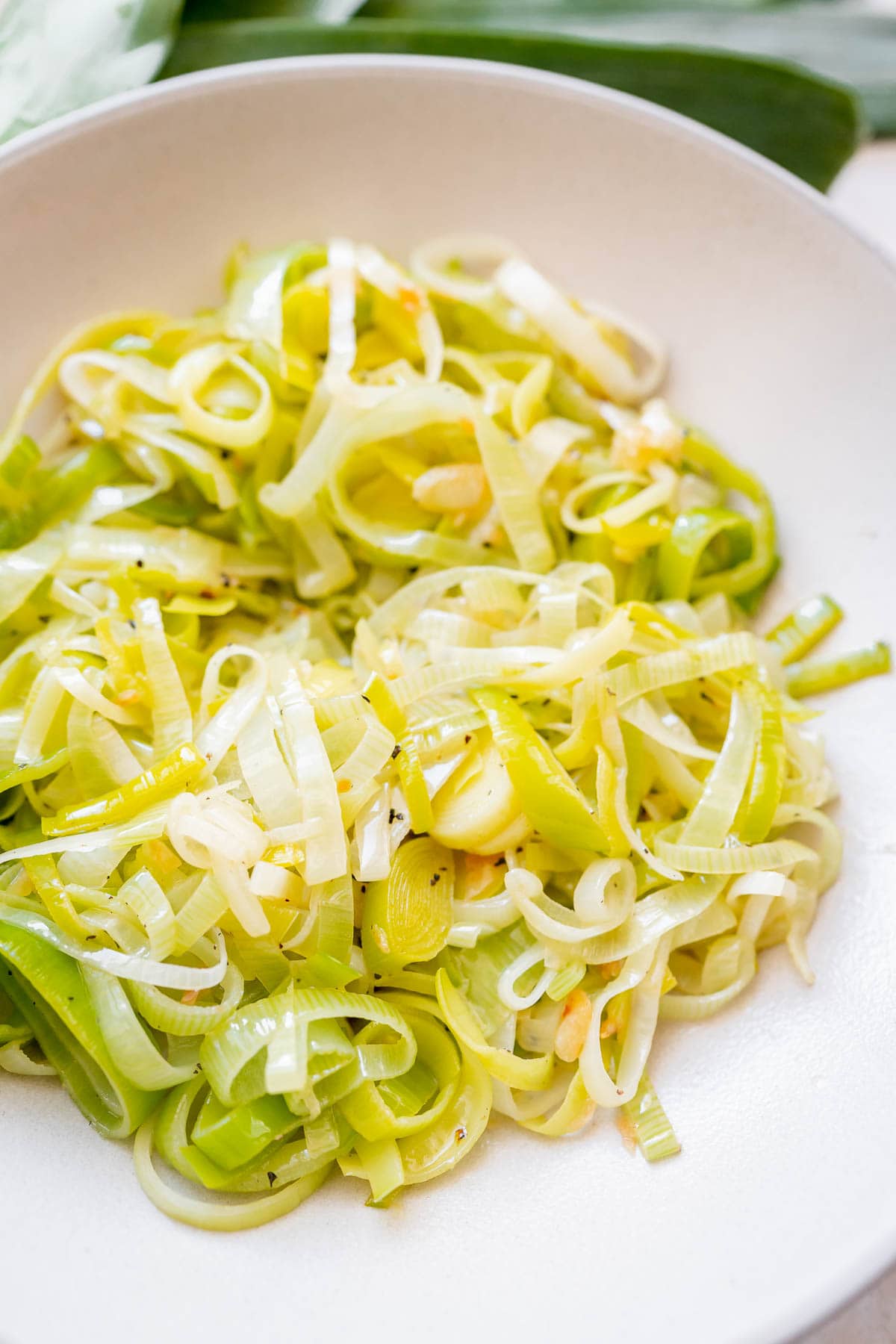 Close shot of freshly sauteed leeks in a large ceramic bowl.