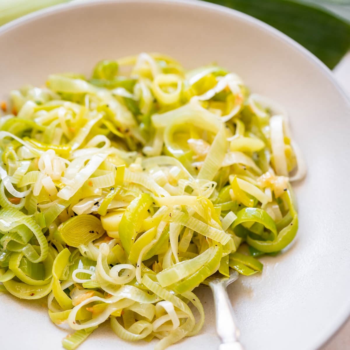 A silver fork rests in a large ceramic bowl of cooked, sliced green leeks.