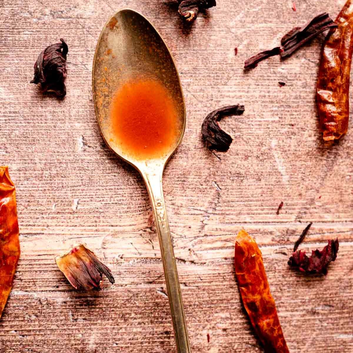 A silver spoon filled with hot sauce resting on a wooden table.