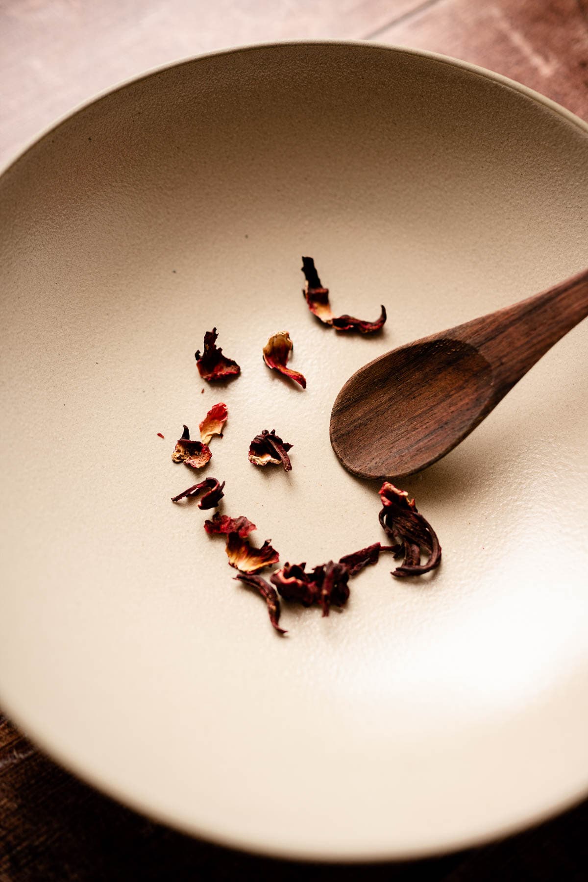 A tan ceramic bowl filled with dried hibiscus flowers.