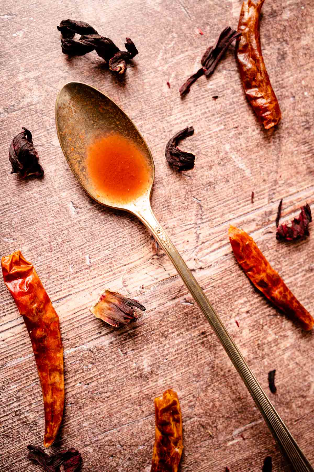 Close shot of a tarnished silver spoon filled with orange red hot sauce resting on a wooden backdrop.