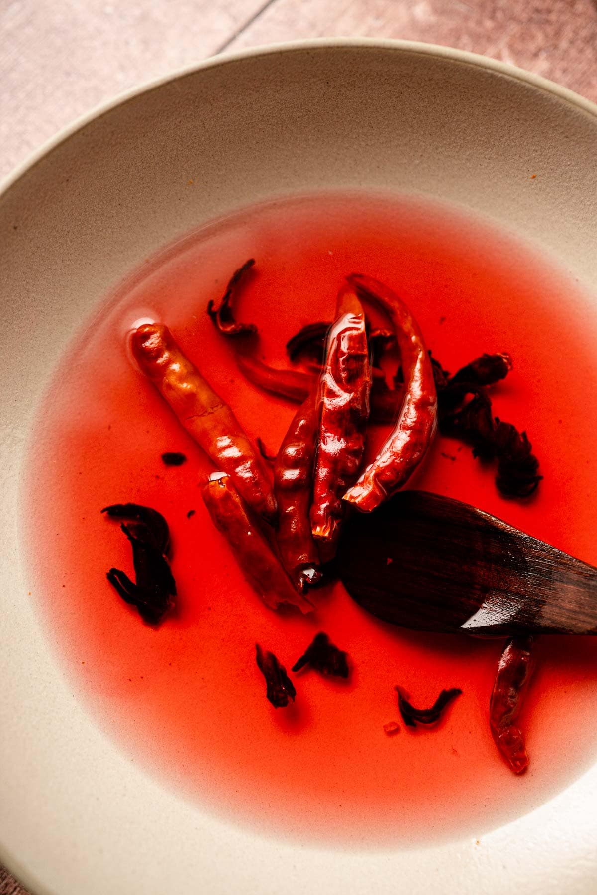 Dried chiles and hibiscus flowers coloring water red in a ceramic bowl.