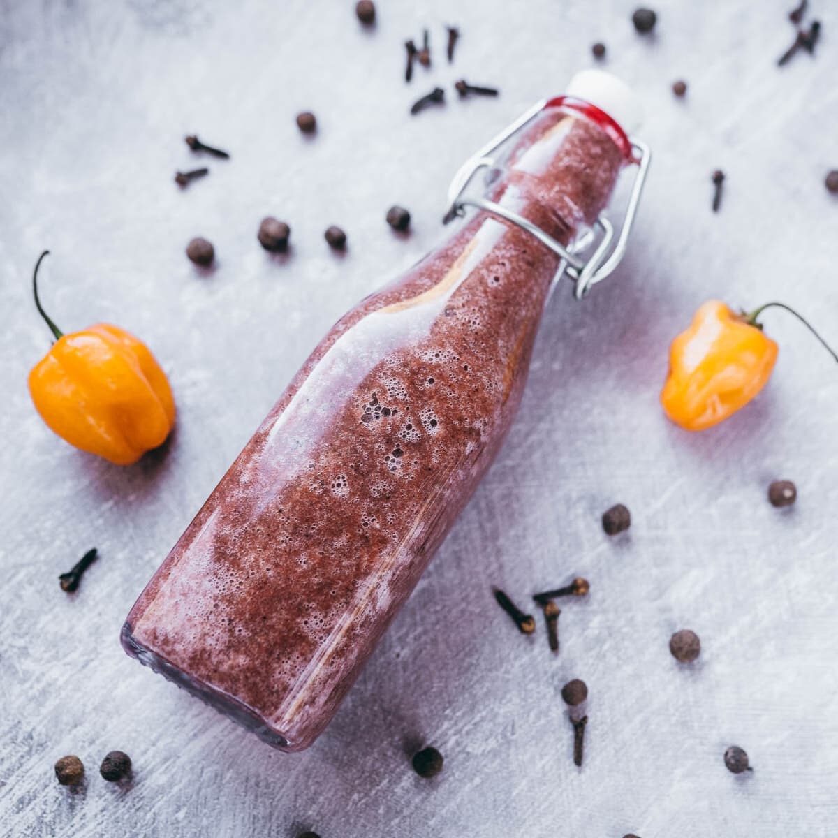 A clear glass hot sauce bottle filled with a dark red sauce.