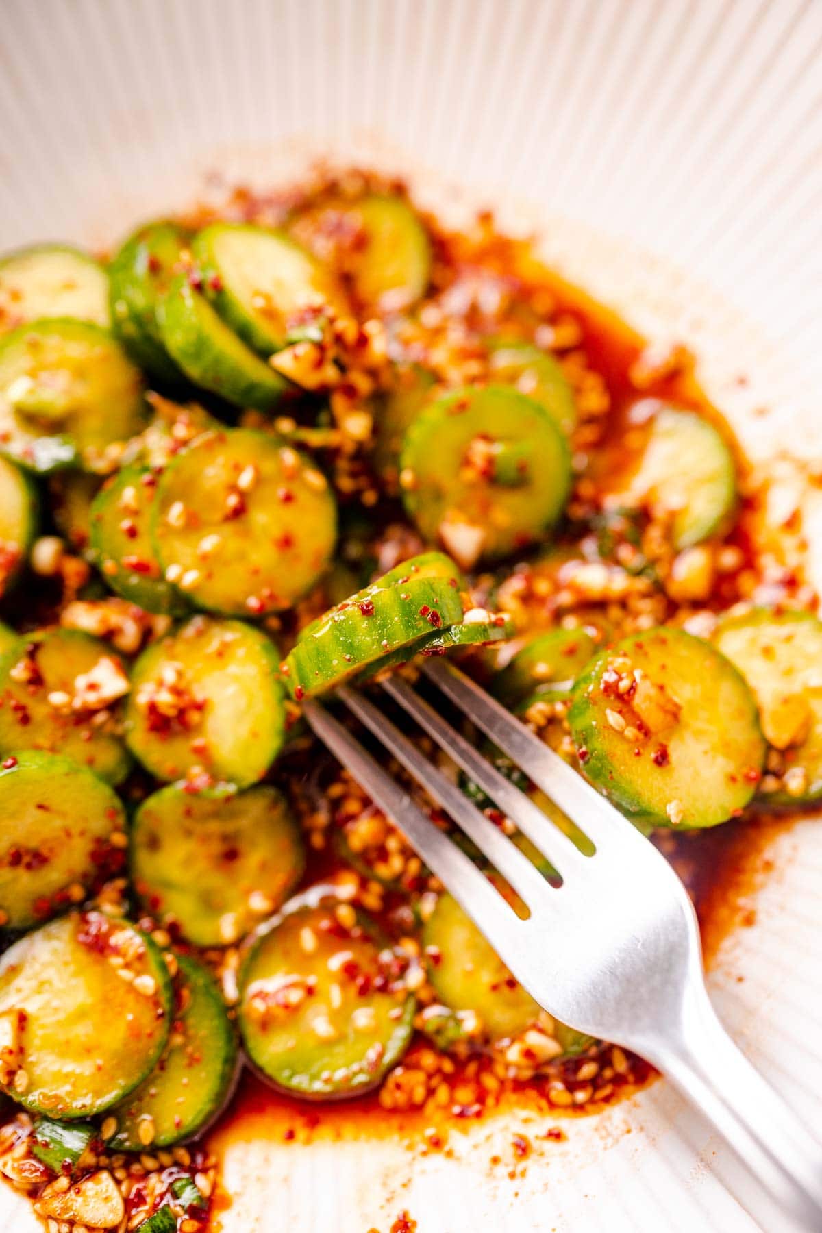 A silver fork holds a cucumber slice coated in chili flakes.