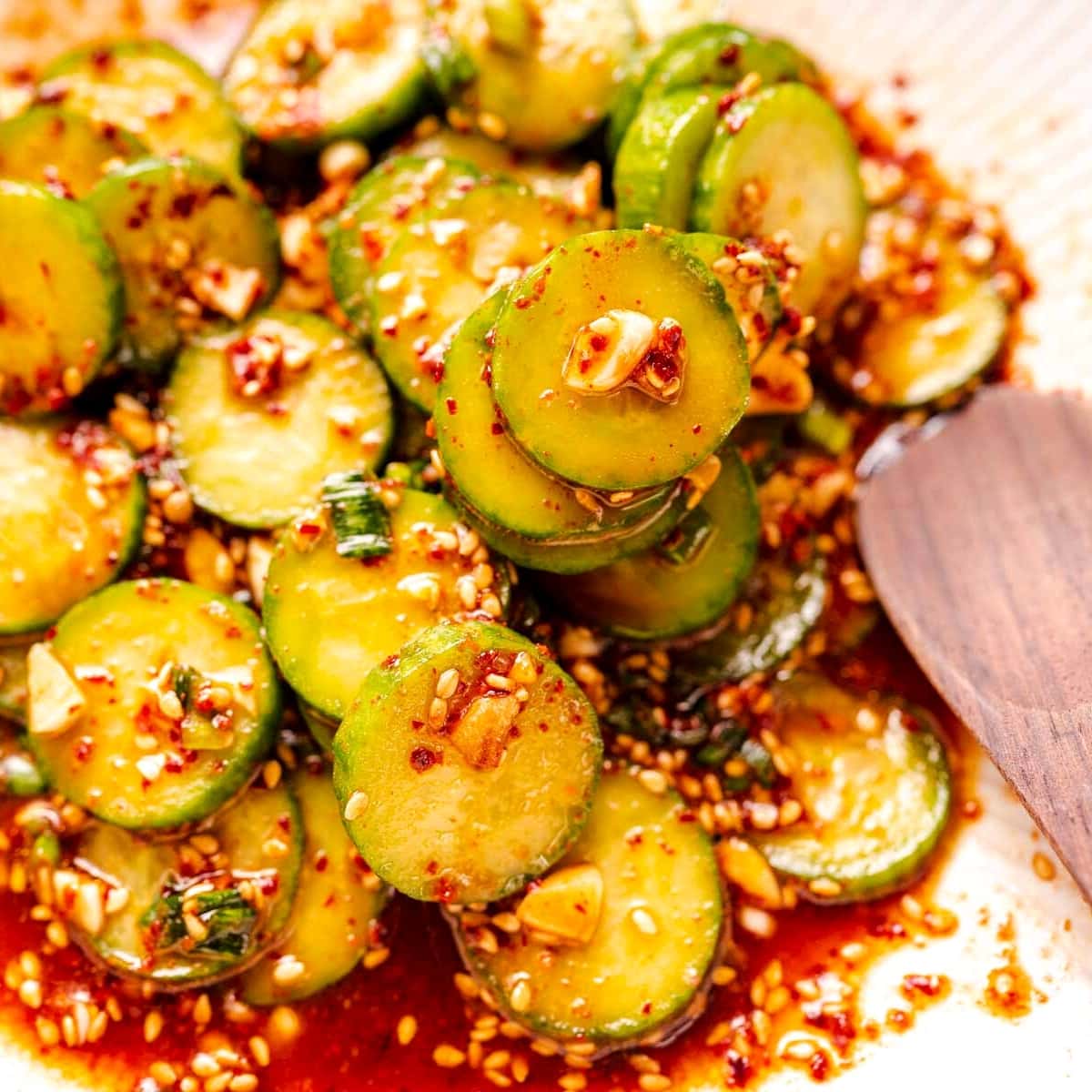 Close shot of sliced cucumbers tossed in a red dressing.