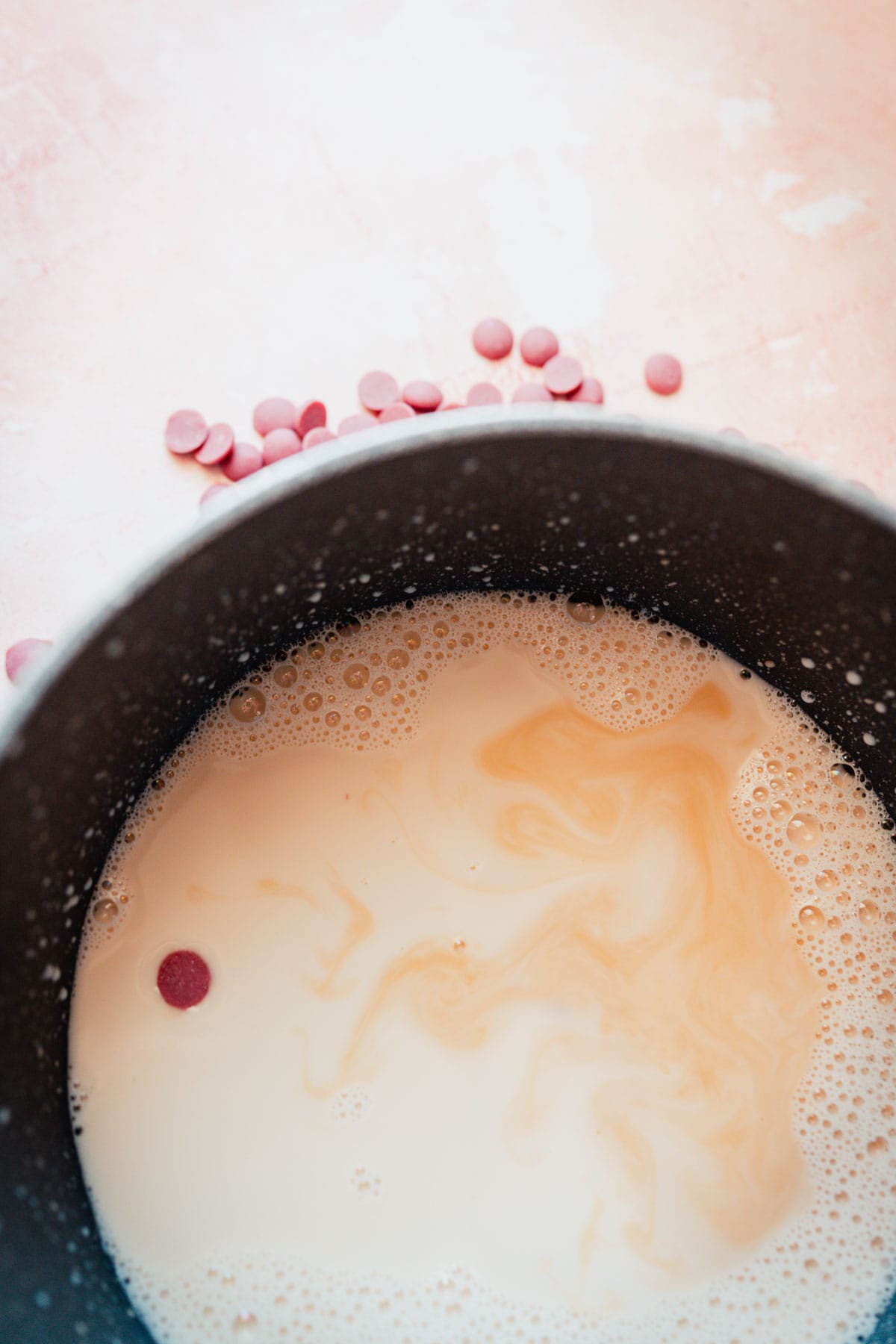 A dark gray saucepan filled with white milk and pink chocolate chips.