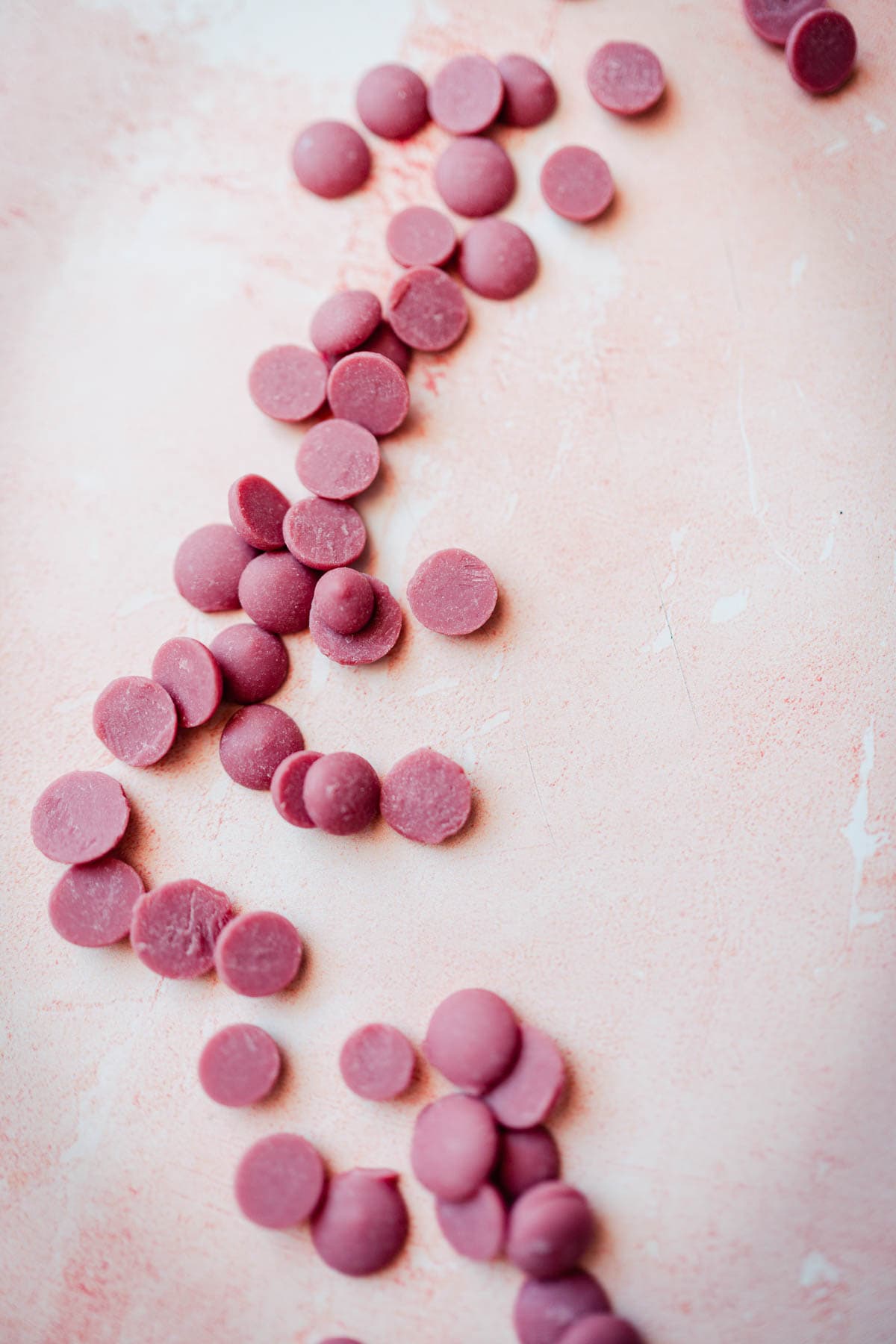 Ruby chocolate chips scattered on a pink table.