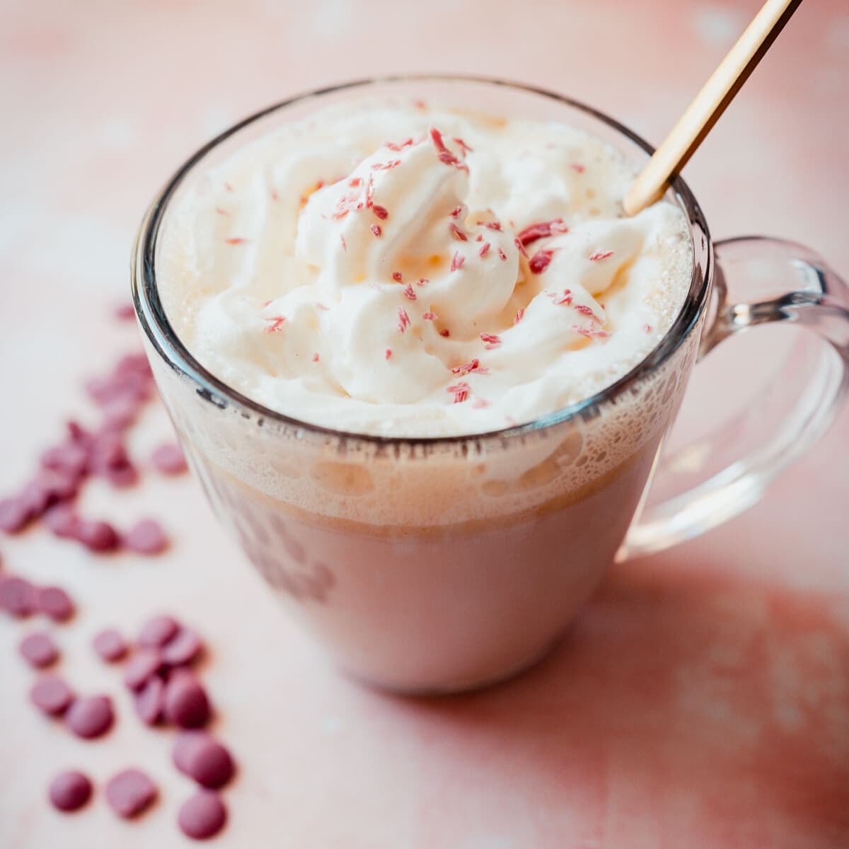 Close shot of a clear glass mug filled with ruby hot chocolate and topped with whipped cream and ruby chocolate shavings.