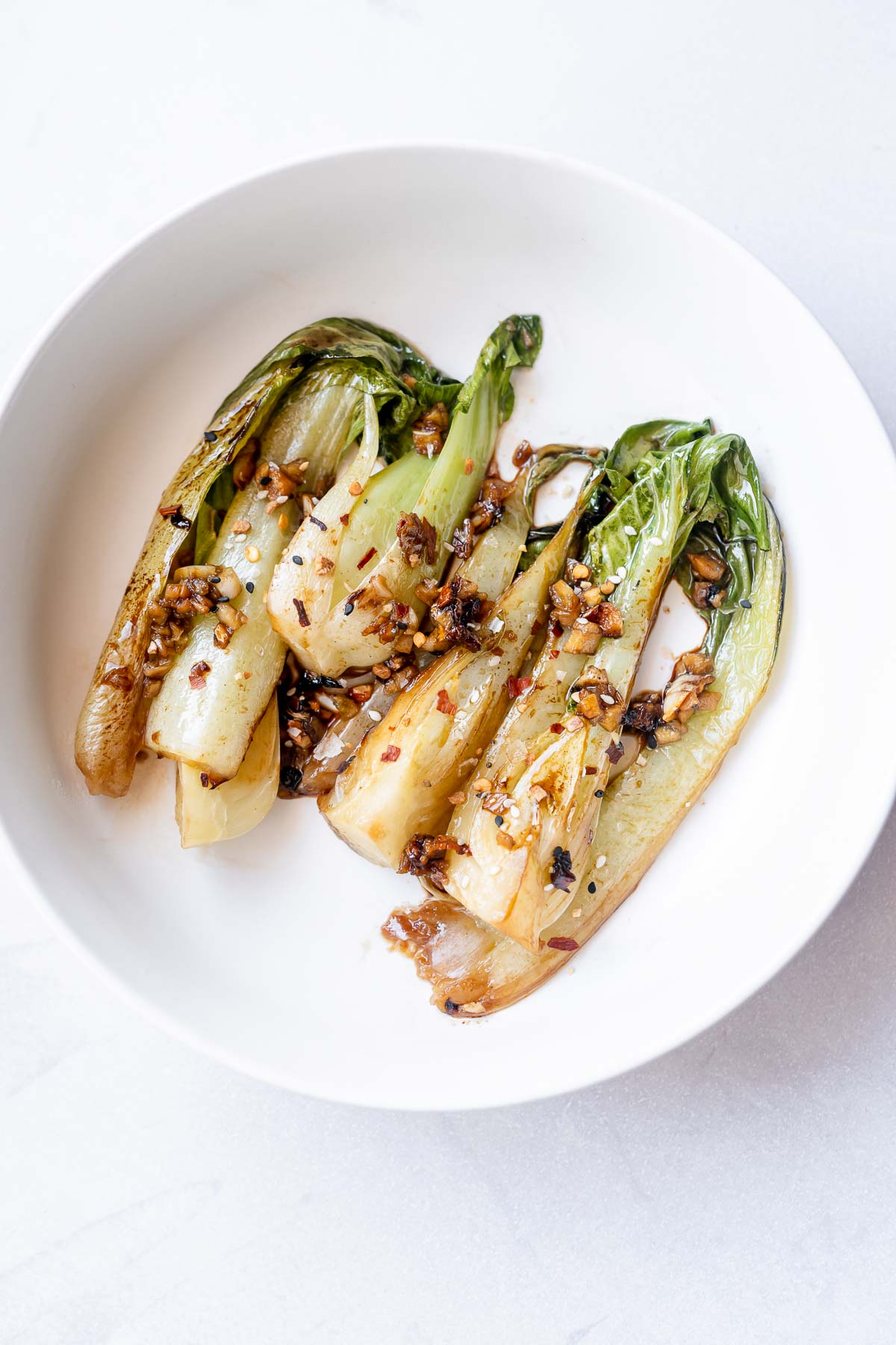 A white bowl with wilted bok choy with cooked garlic and spices.