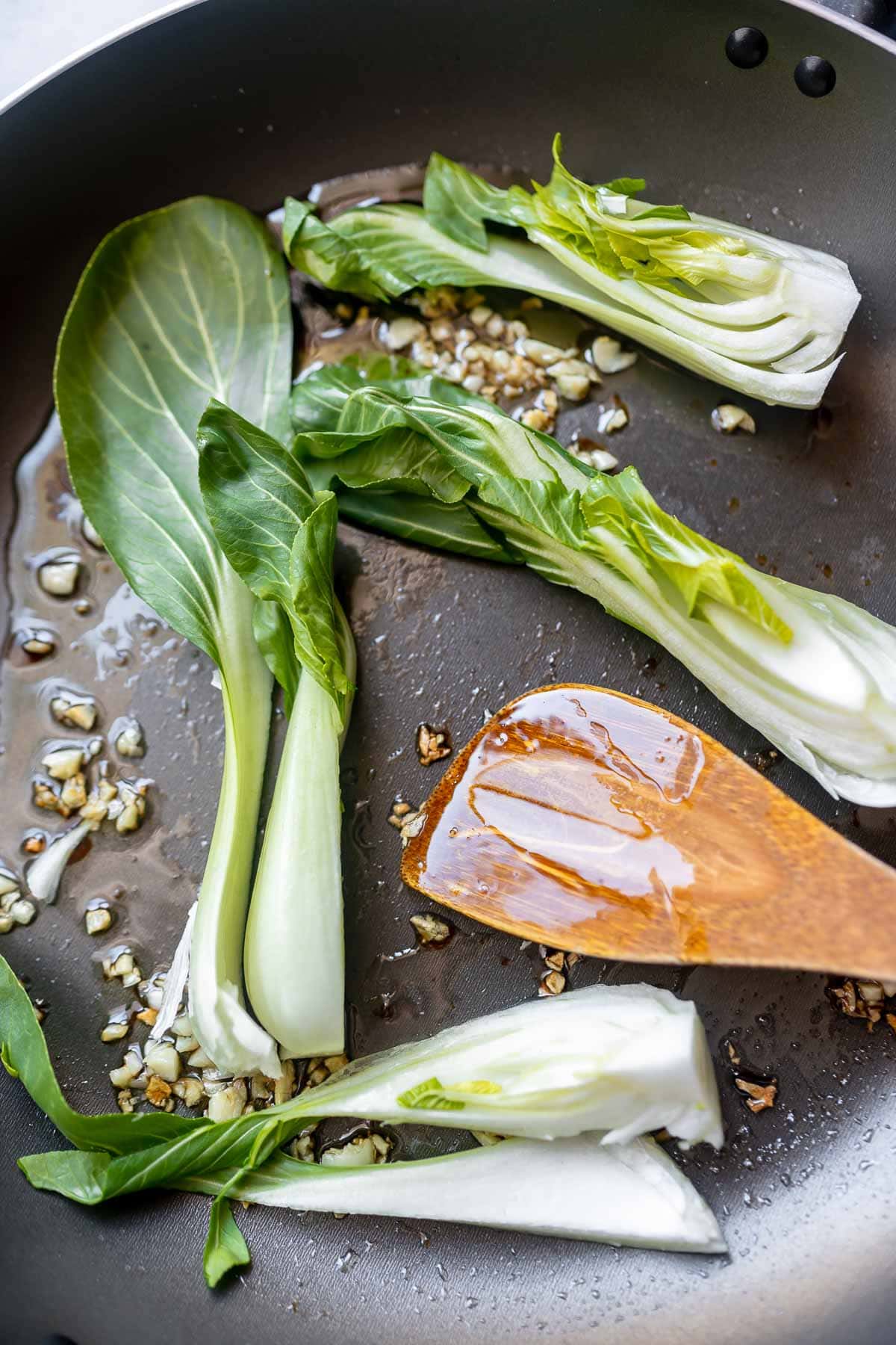 A skillet with bok choy, garlic and oil.