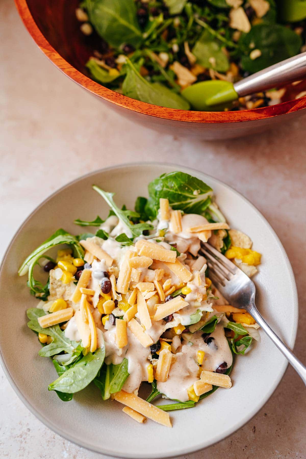 A ceramic bowl of salad resting next to a wooden salad bowl.