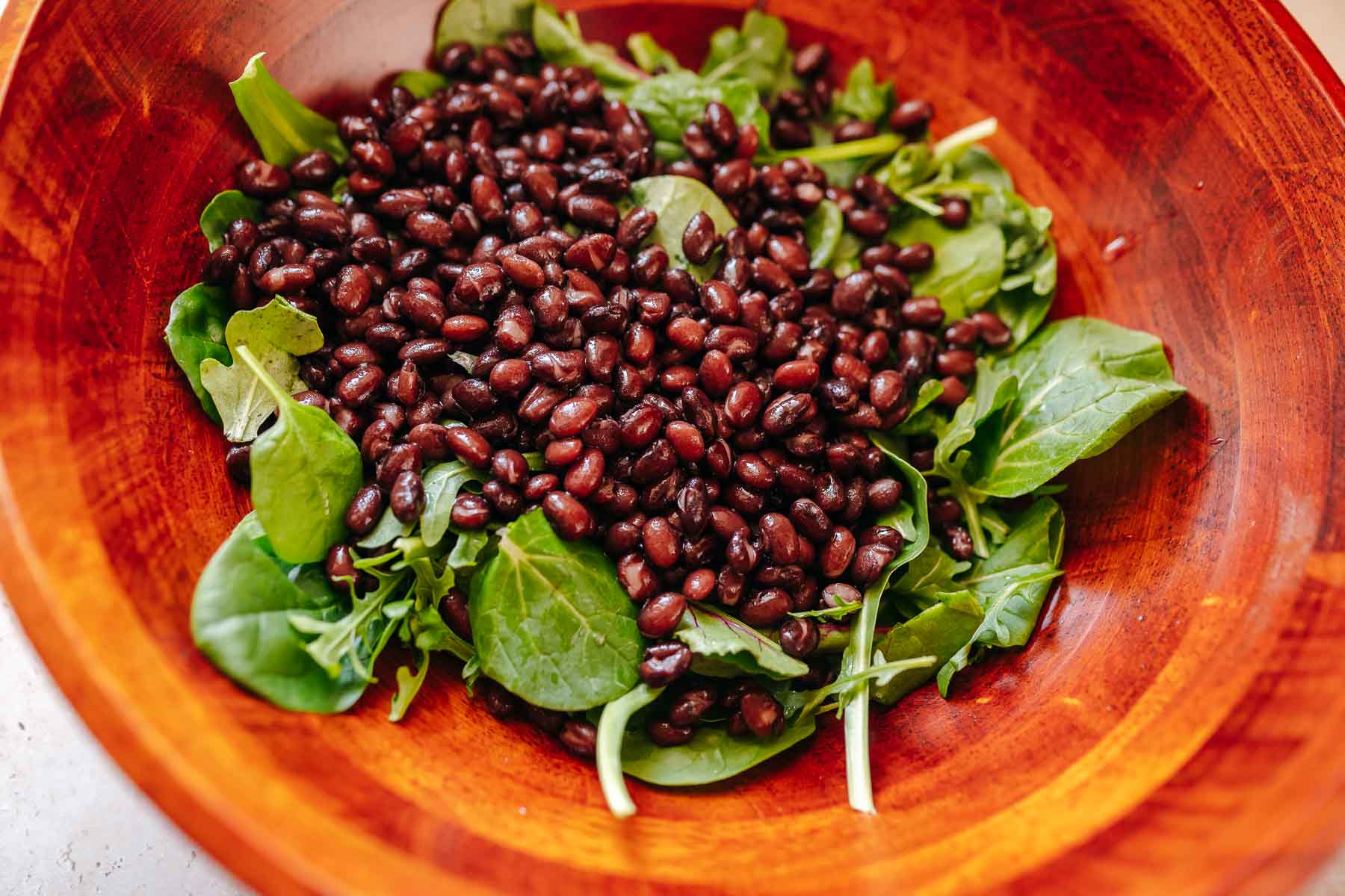 A wooden salad bowl filled with greens and black beans.