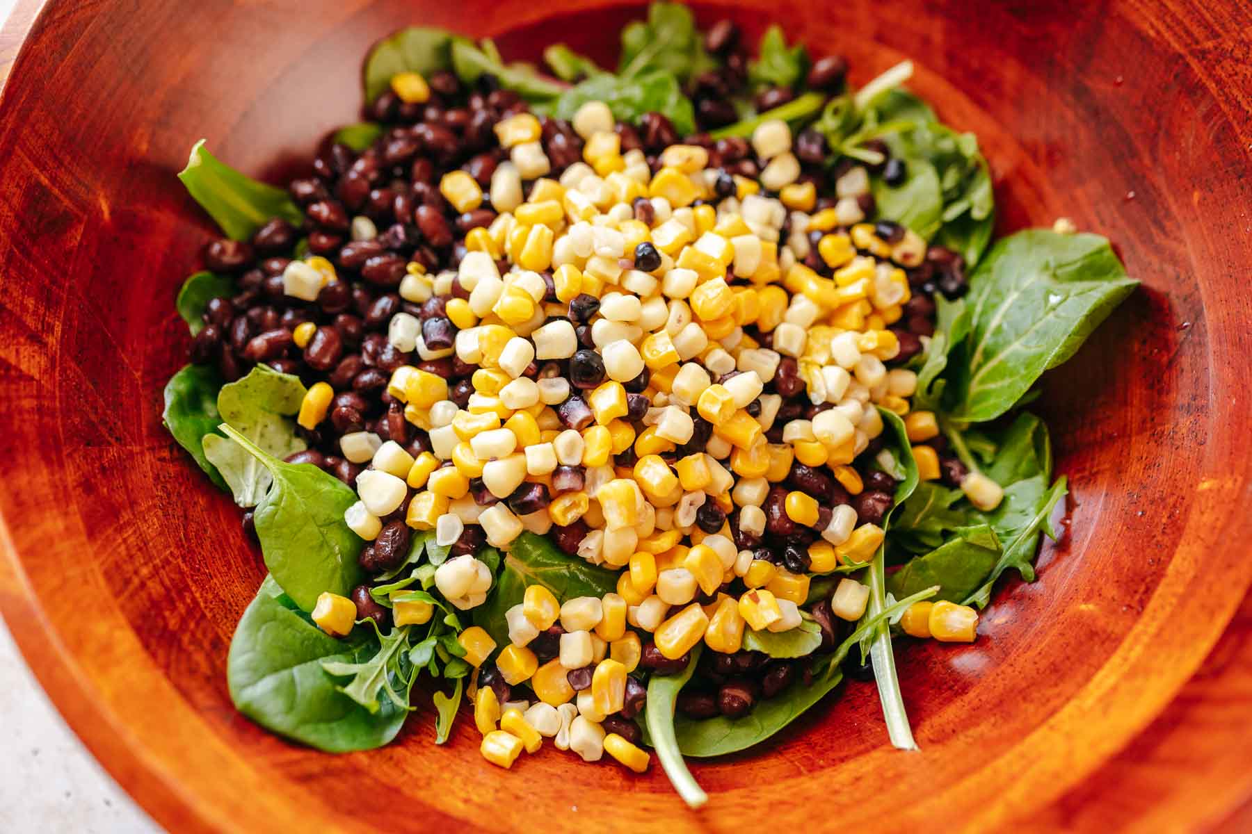 A red wooden salad bowl filled with greens, beans and corn.