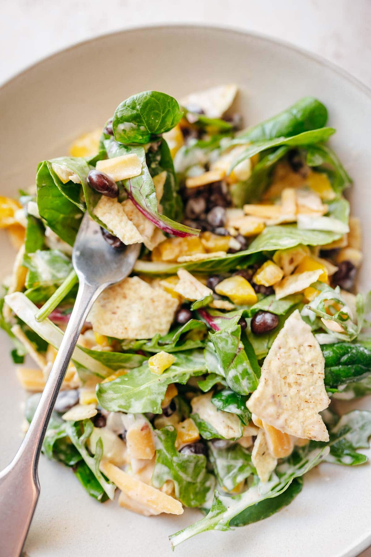 A close shot of a southwest salad topped with tortilla chips and a silver fork.