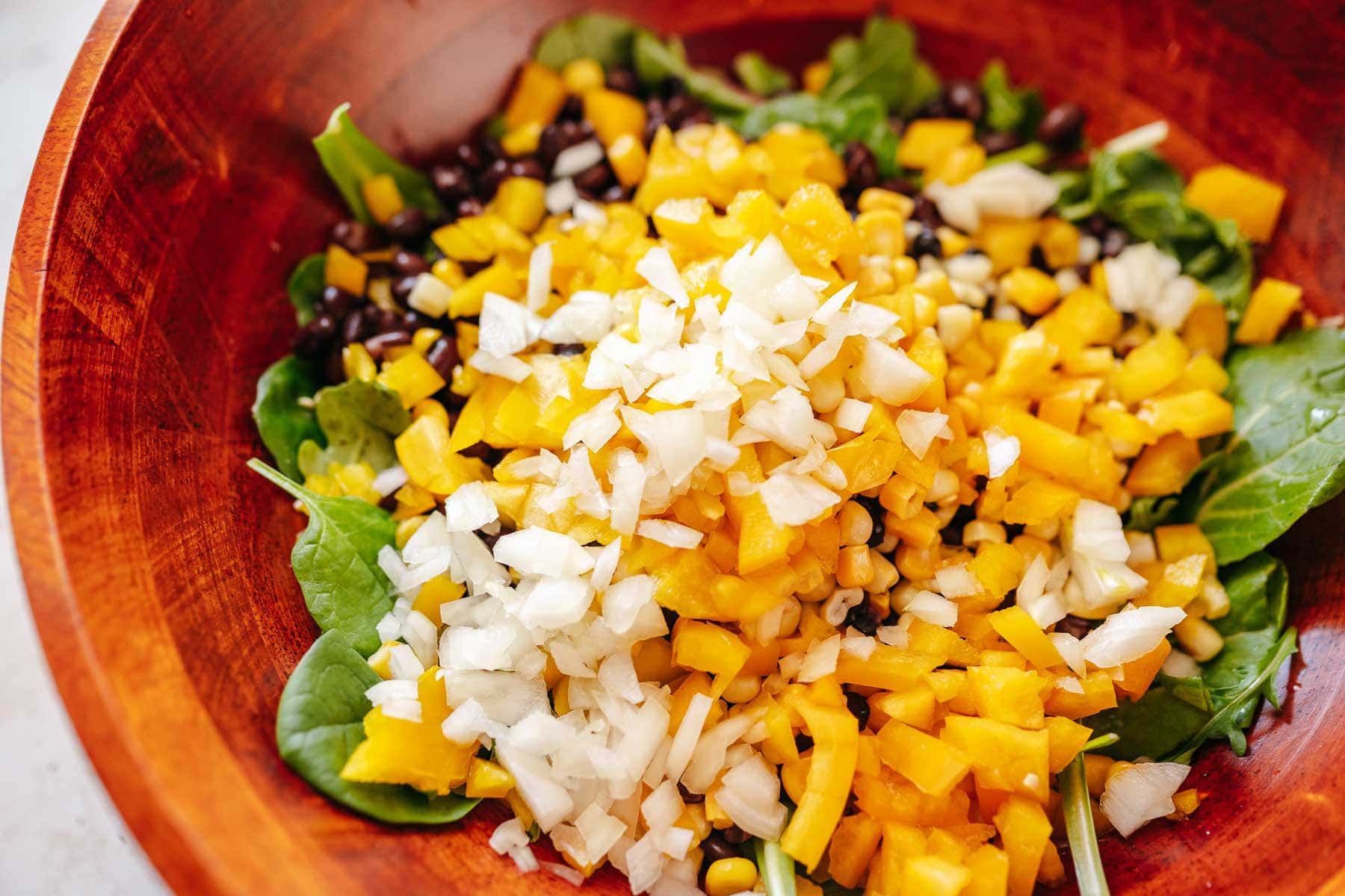 A large wooden salad bowl filled with greens. corn, onions and beans.