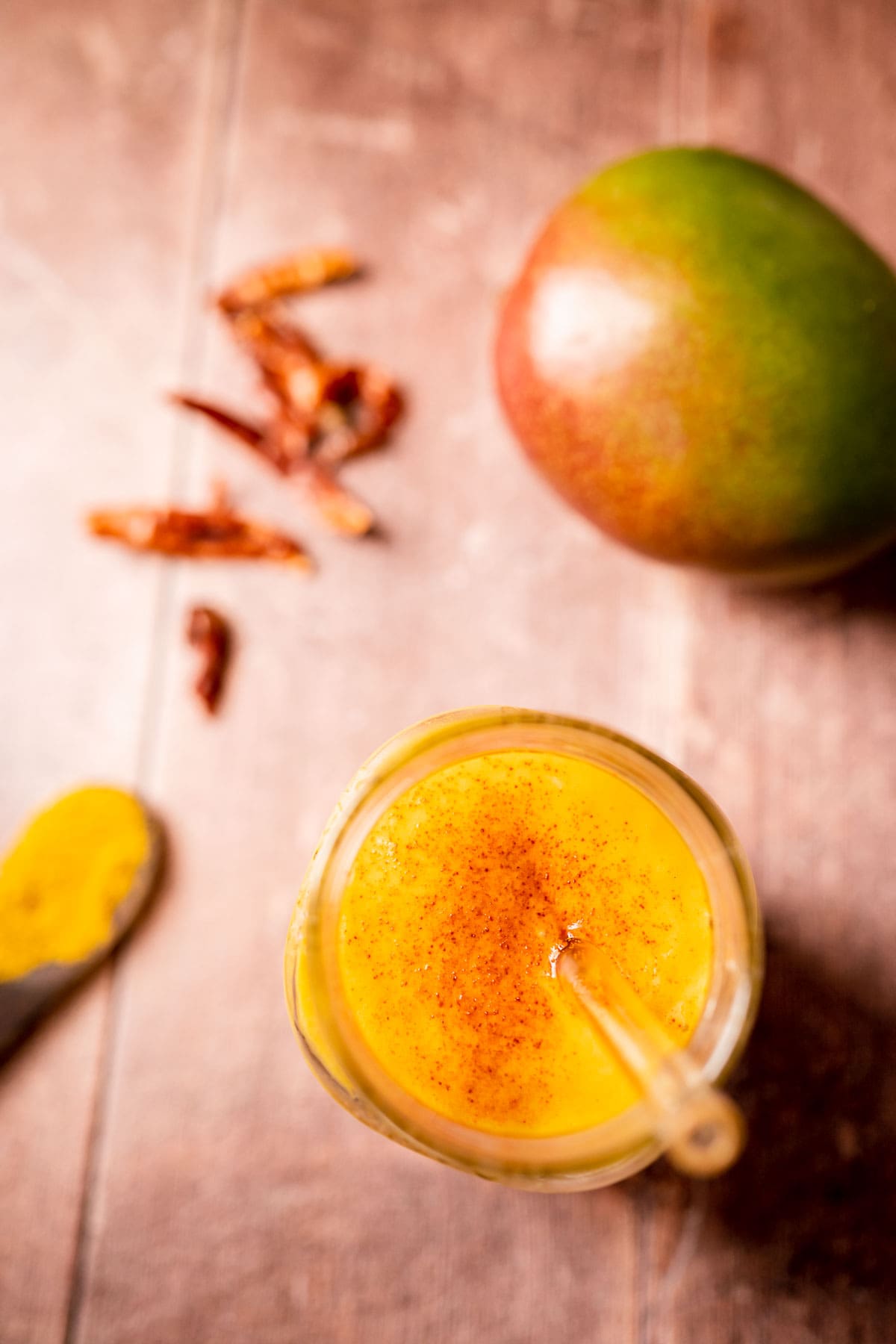 Close view of mango golden milk smoothie garnished with ground cayenne.