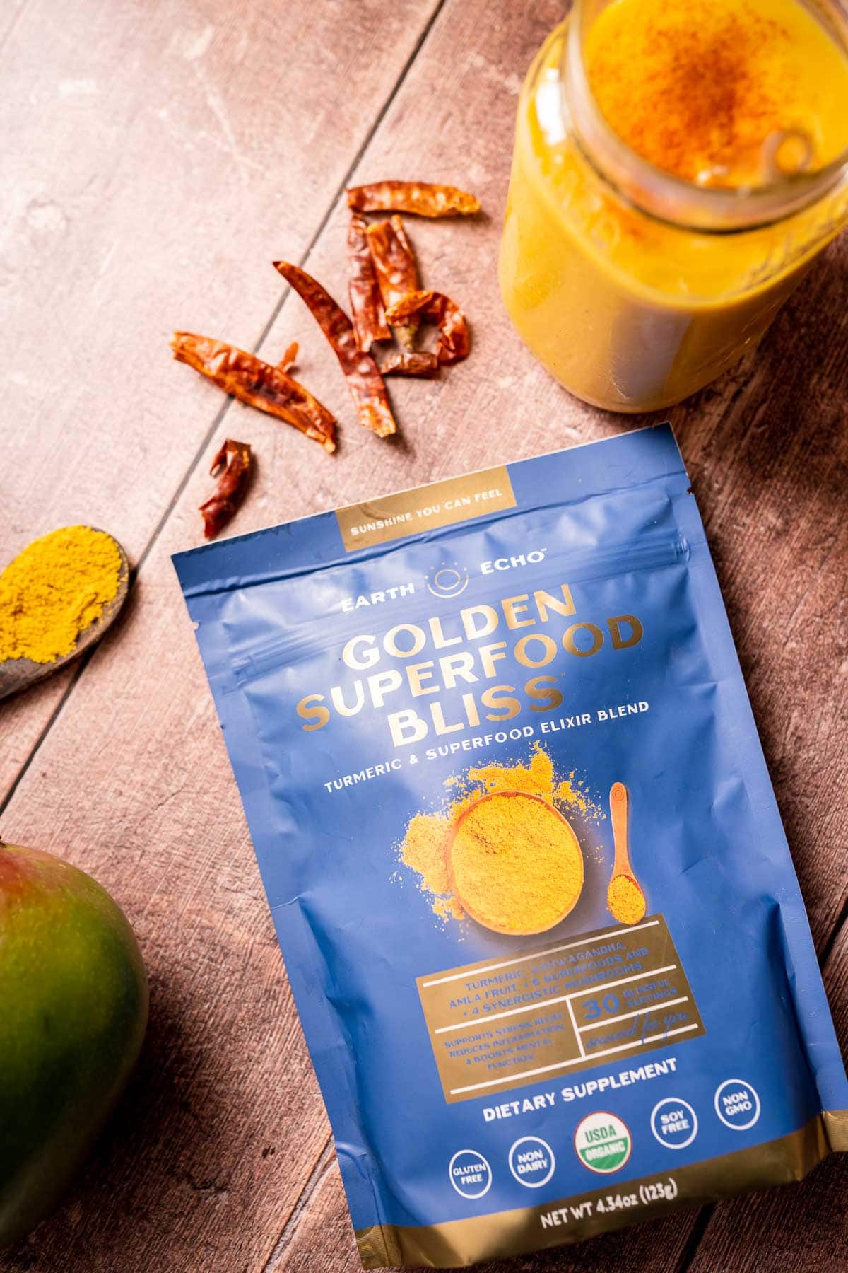 A blue bag of Earth Echo Golden Superfood Bliss resting on a wooden table alongside other ingredients.