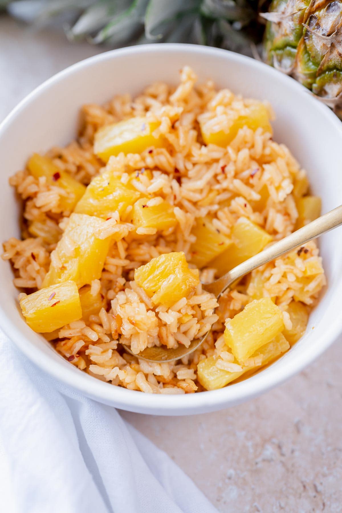 Close shot of a silver spoon holding pineapple rice over a white bowl.