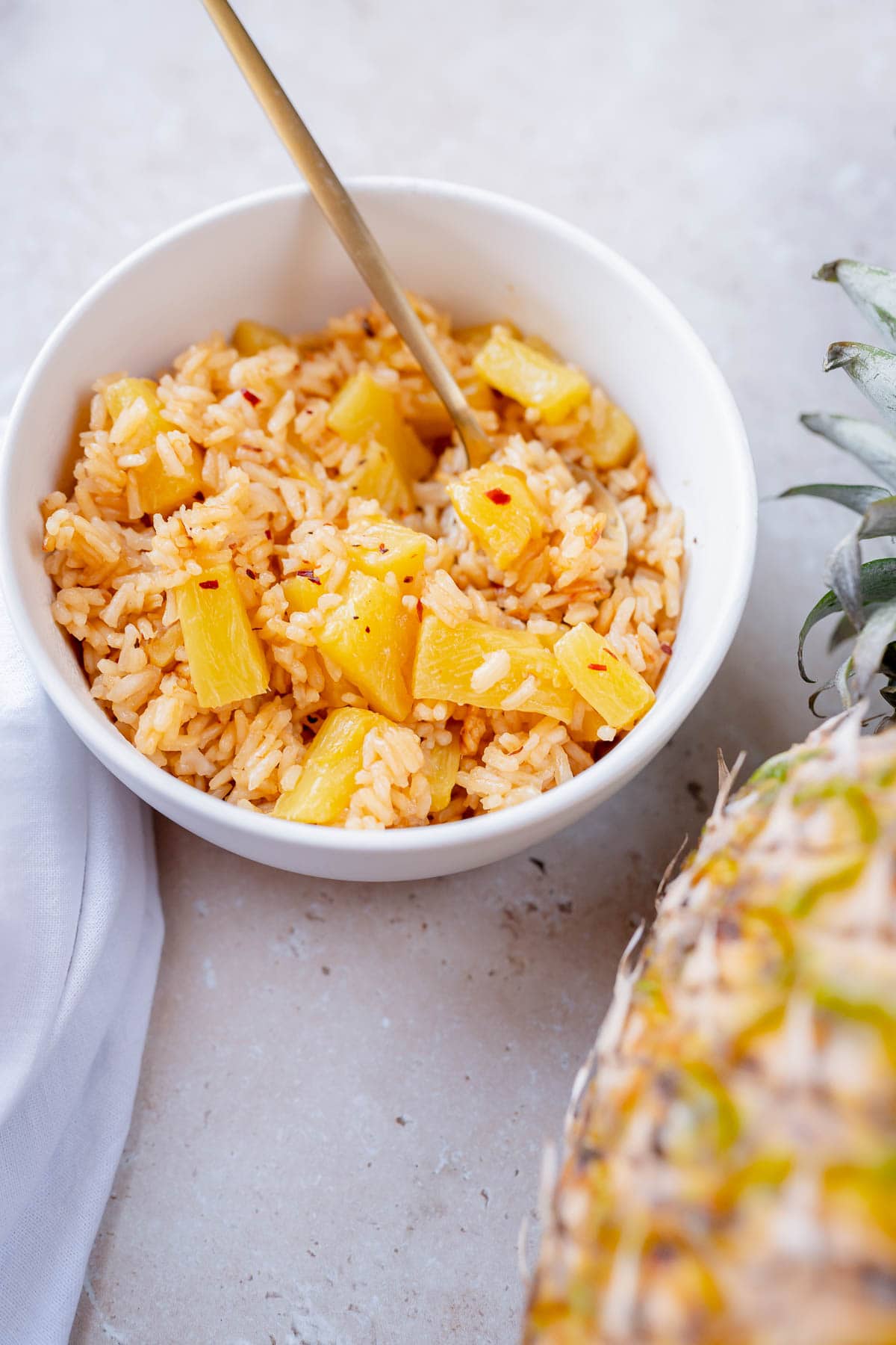 A white bowl filled with white rice, pineapple chunks and red chili flakes.