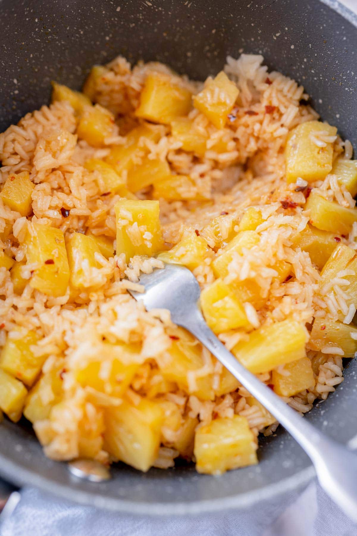 A silver fork fluffs a pan of pineapple rice.