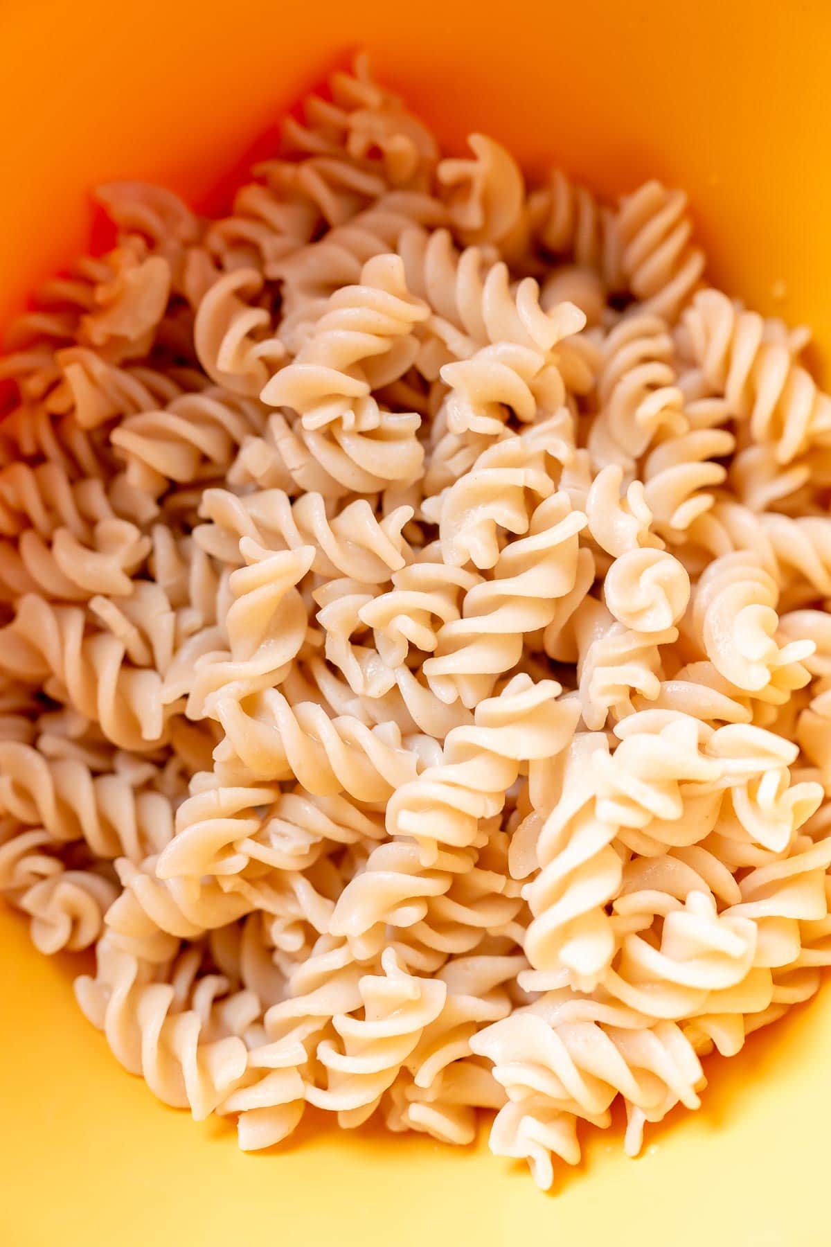 A yellow bowl of cooked fusilli pasta noodles.