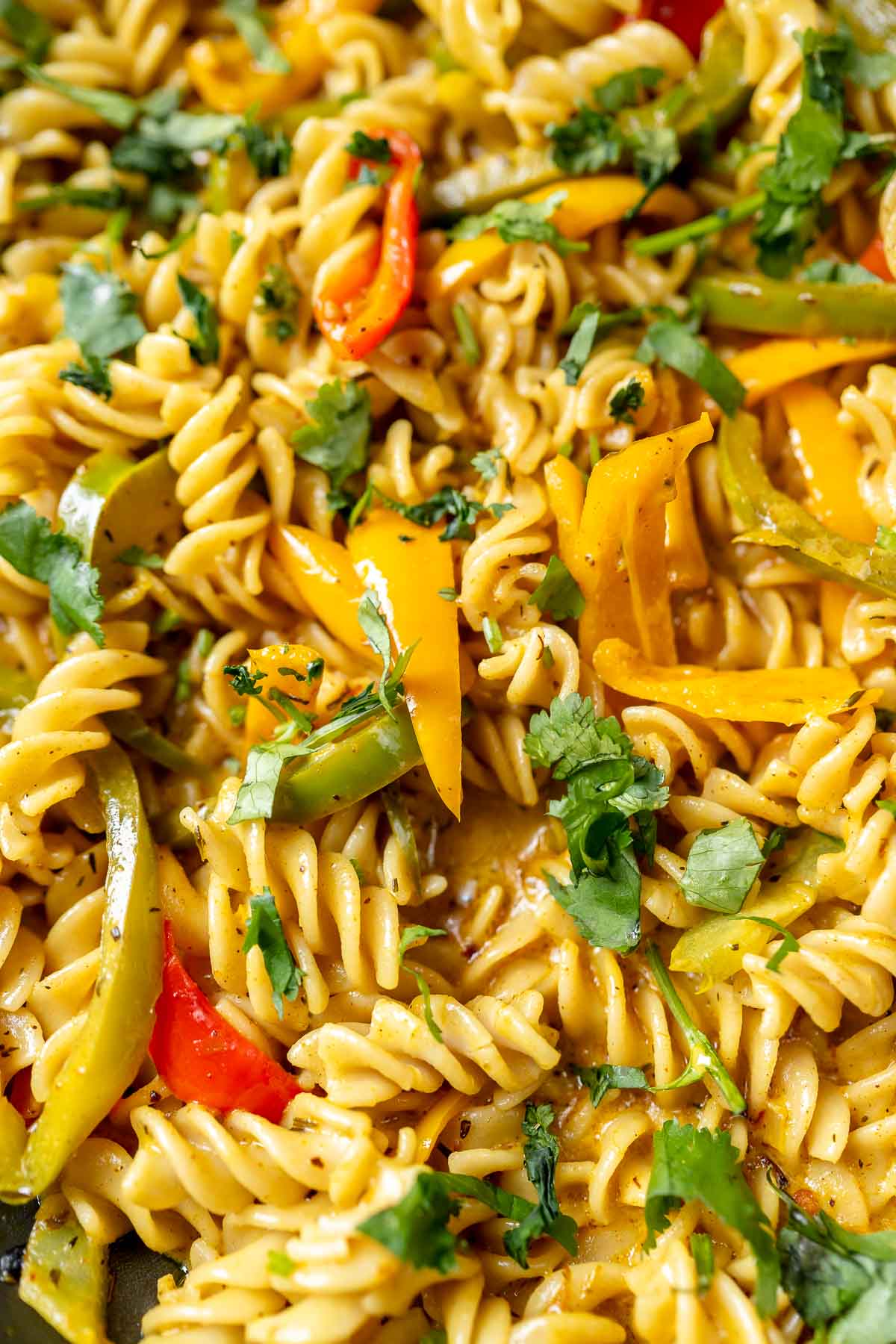 Close shots of creamy yellow noodles topped with sliced bell pepper strips and fresh green herbs.