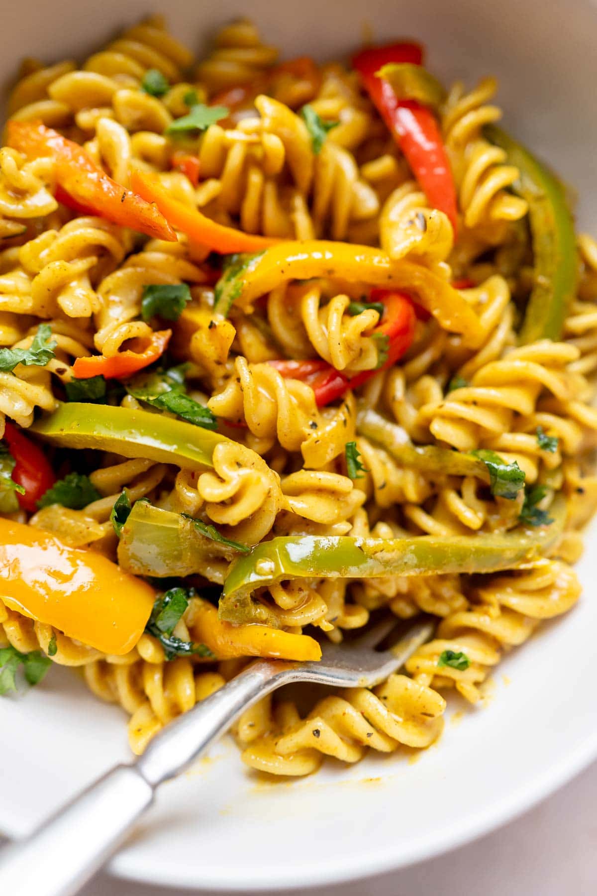 A close shot of a creamy, yellow-colored pasta dish dotted with several colors of sliced bell peppers.