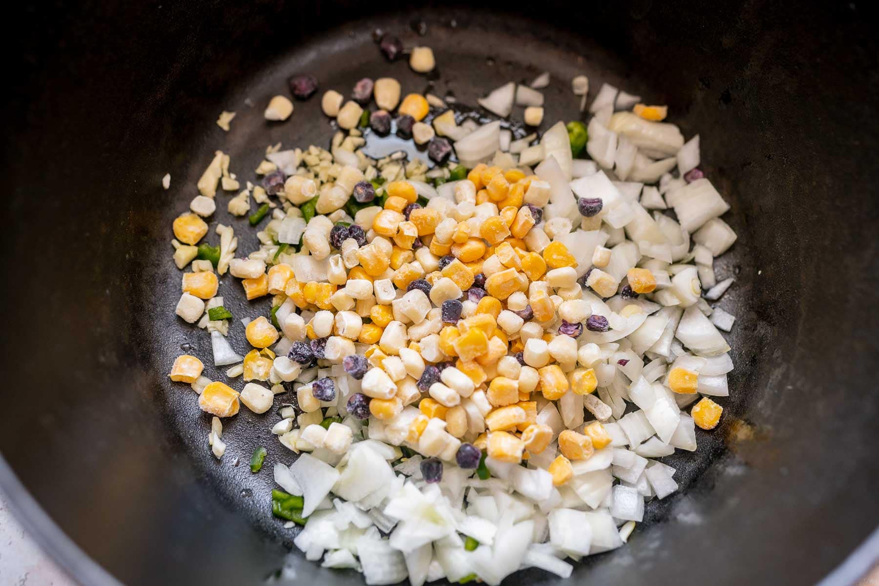 A black pot with chopped onions and corn.