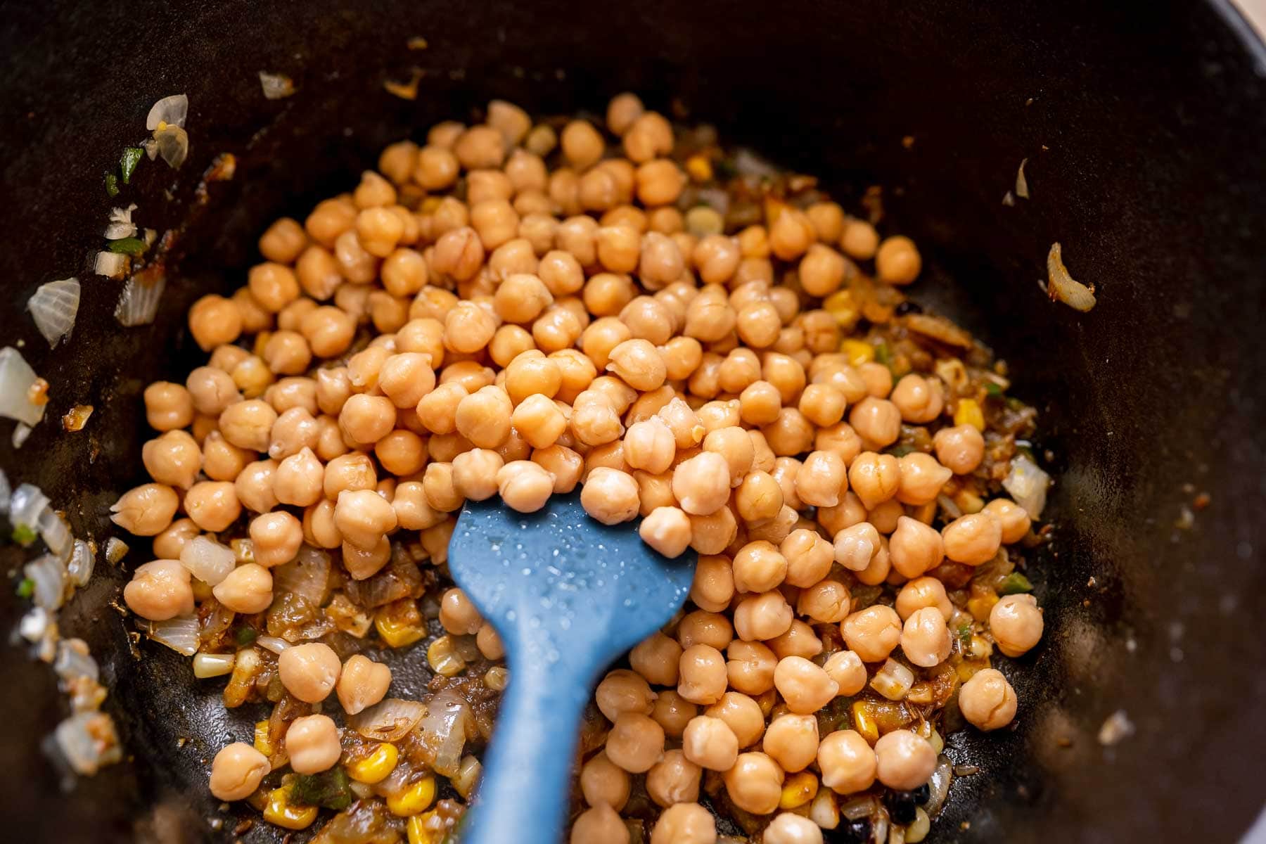Chickpeas in a pot with a blue silicone spatula.