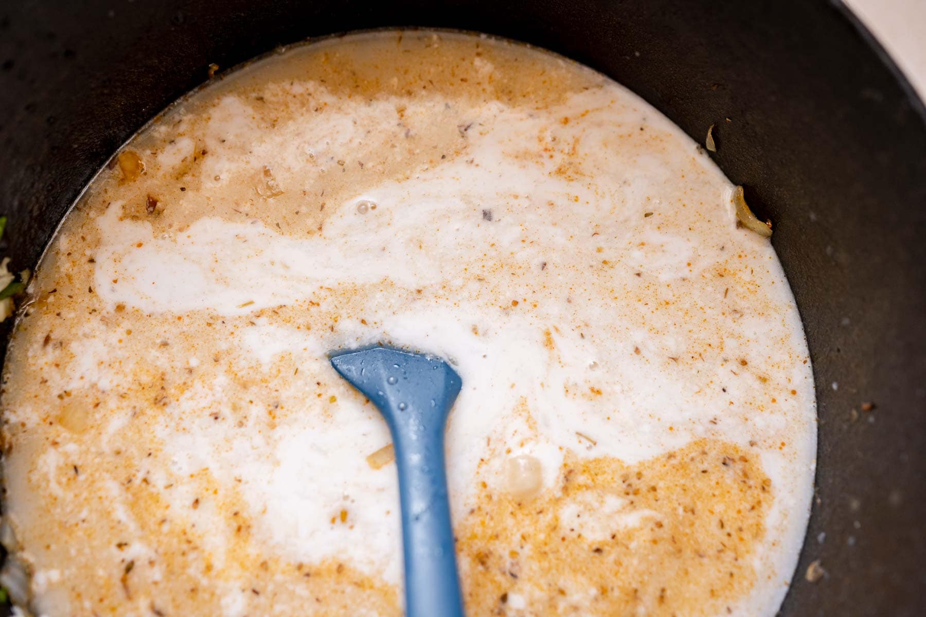 A blue spatula mixes liquid ingredients in a large pot.