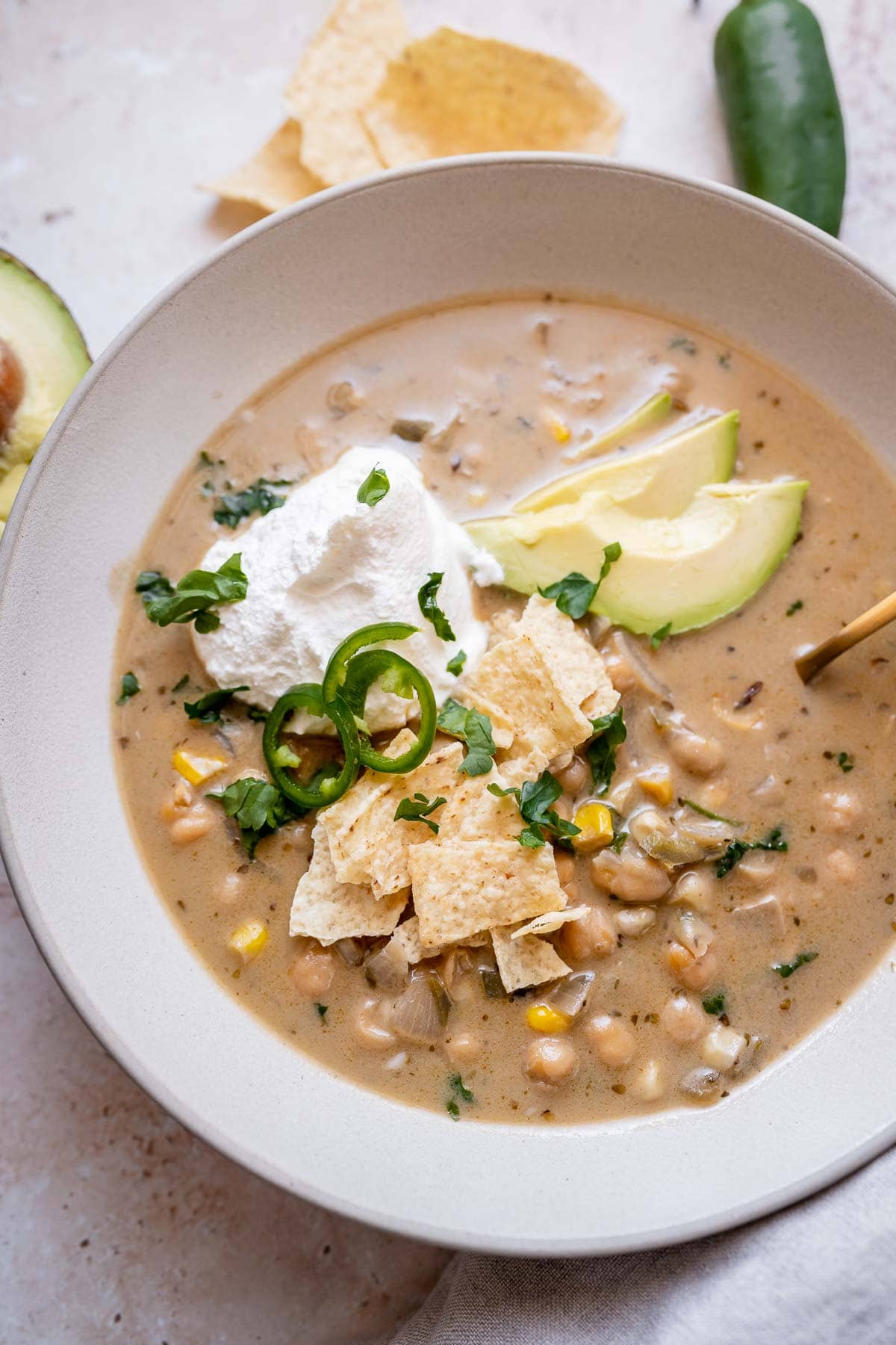 A large ceramic bowl of vegan white chili with fresh herbs, avocado, vegan sour cream and sliced peppers.