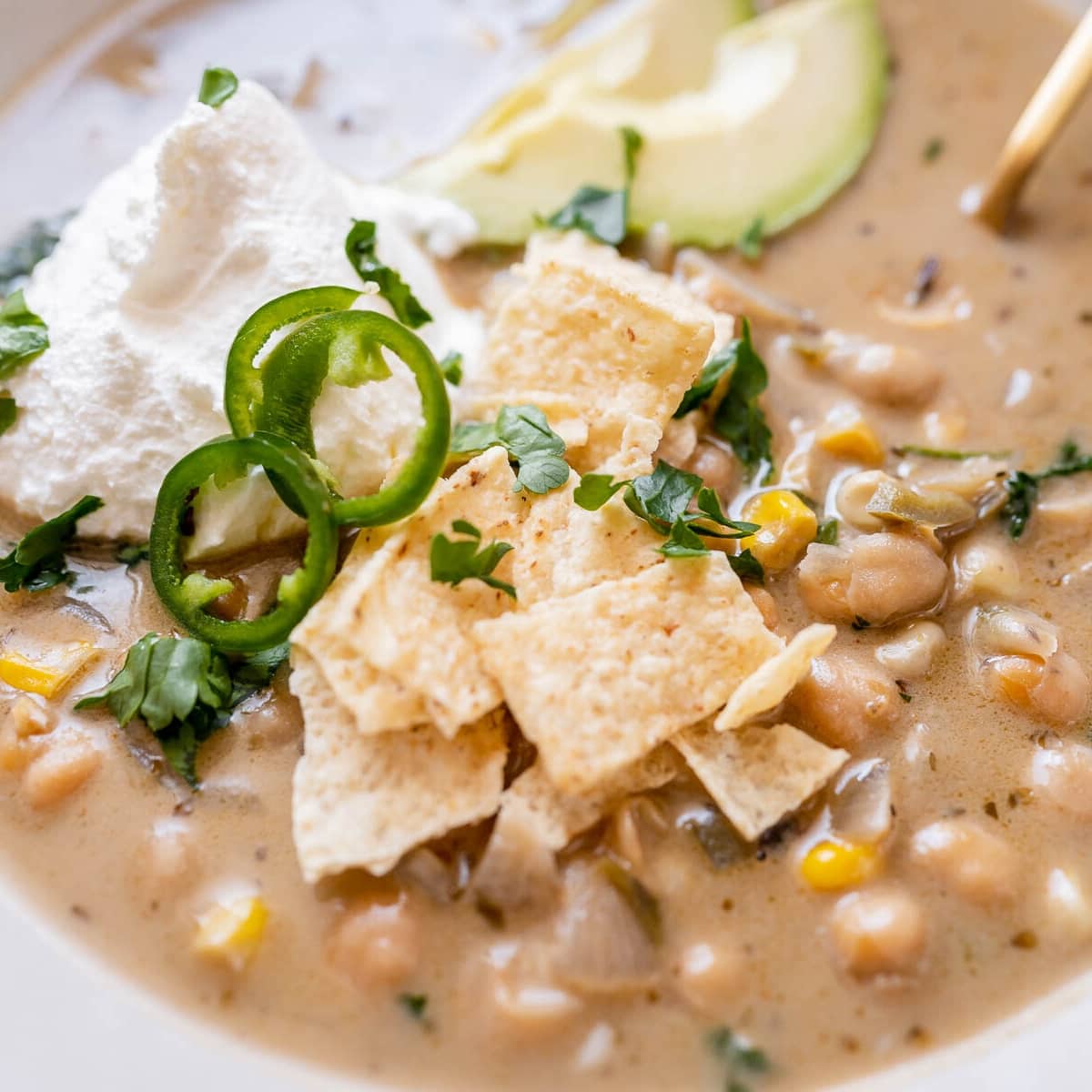 Close shot of a white chili with tortilla chips sliced jalapeno peppers, corn, sour cream and fresh cilantro.