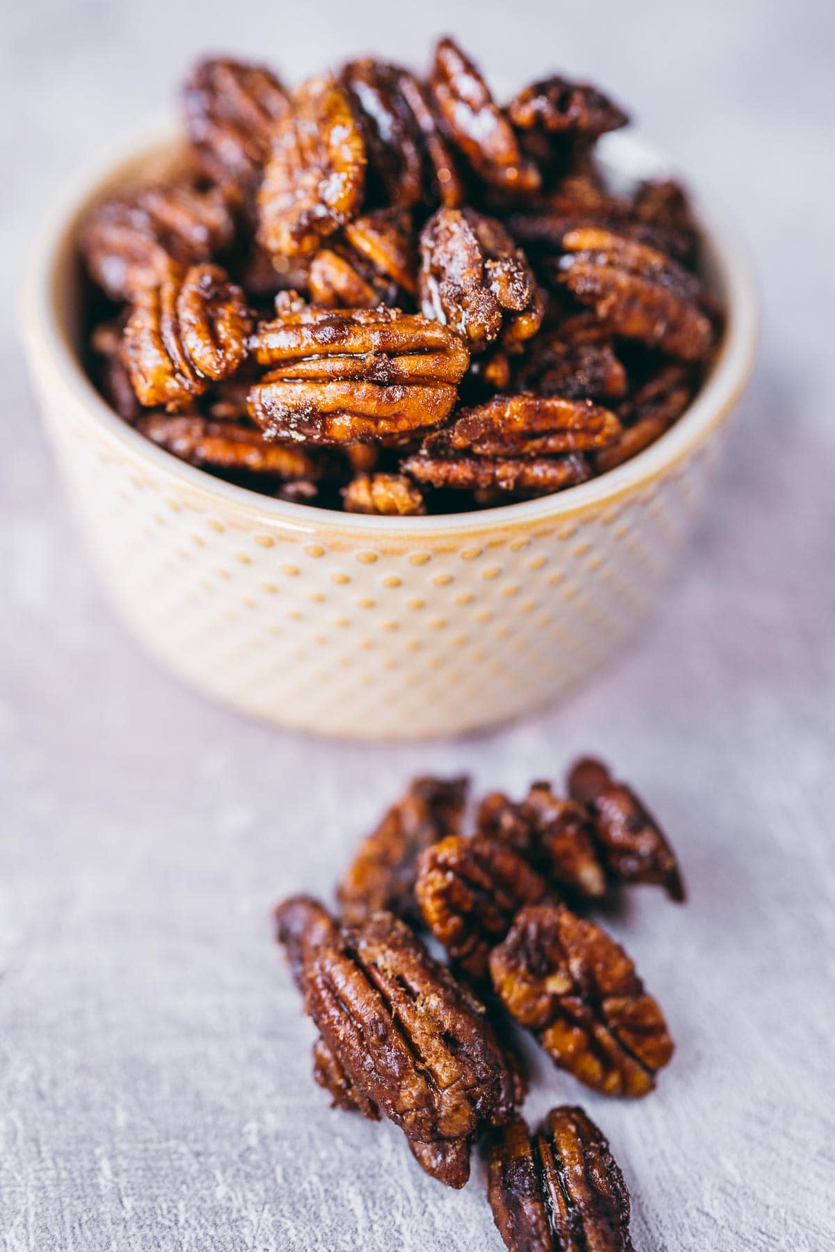 A small tan ceramic bowl filled with homemade candied pecans.