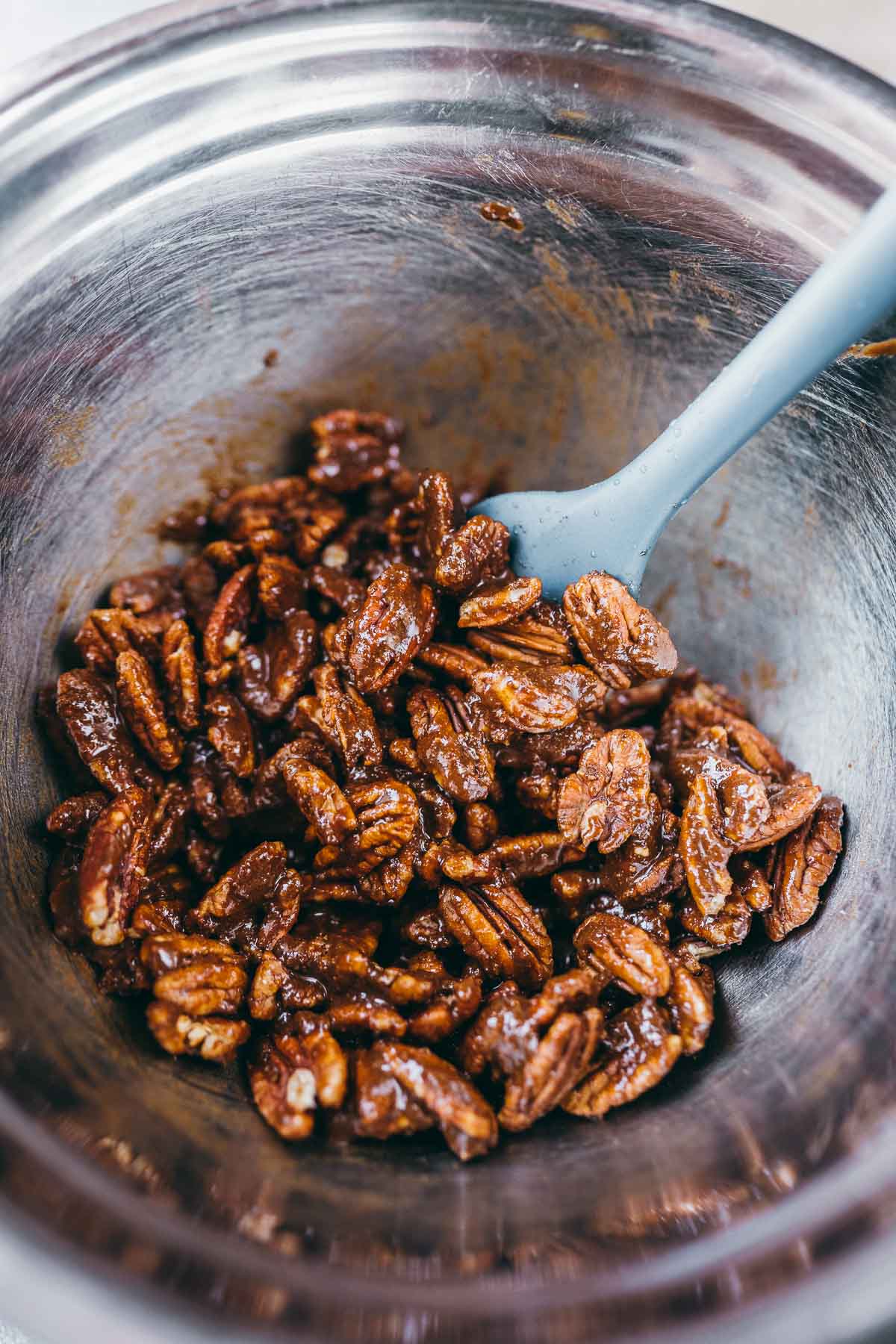 A bowl of pecans being mixed with a sticky liquid.