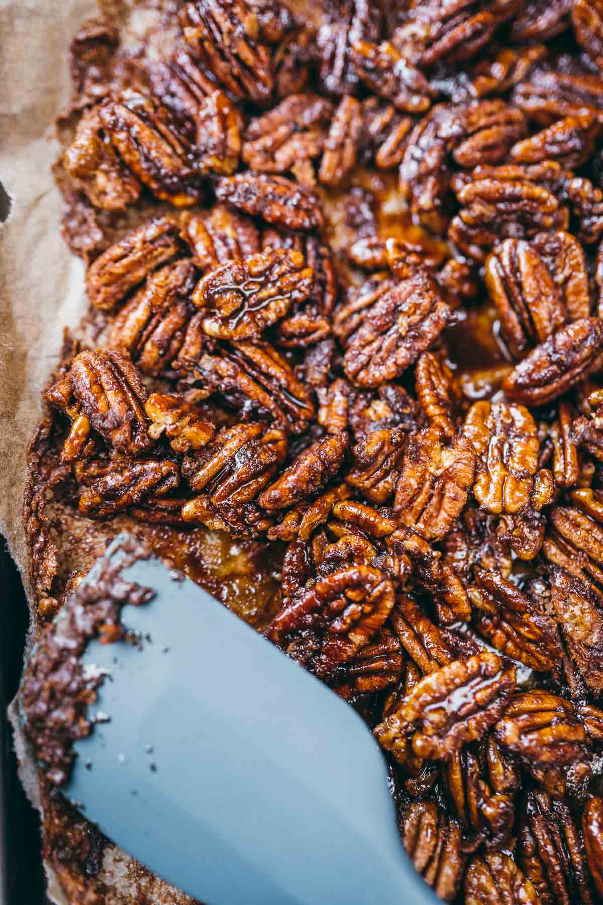A blue spatula rests on a fresh batch of spiced candied pecans.