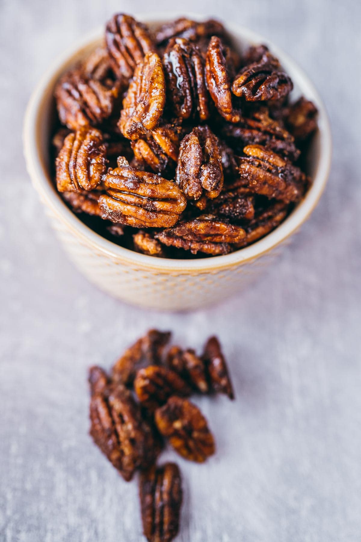 Spicy candied pecans resting in a small ceramic bowl on a gray tabletop.
