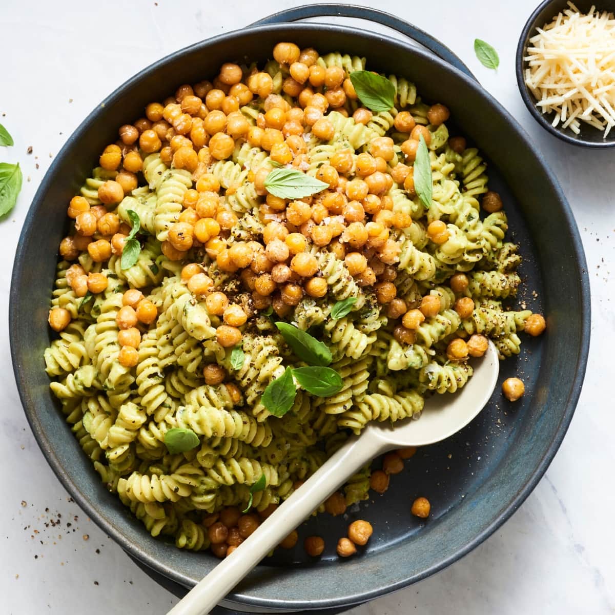 A large black cast iron skillet filled with pasta noodles coated in a green sauce and topped with chickpeas and fresh basil leaves.