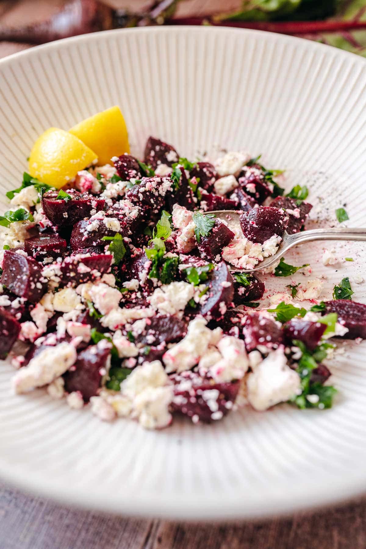 Beet salad with feta cheese and lemon slices resting in a large white bowl with a silver spoon.