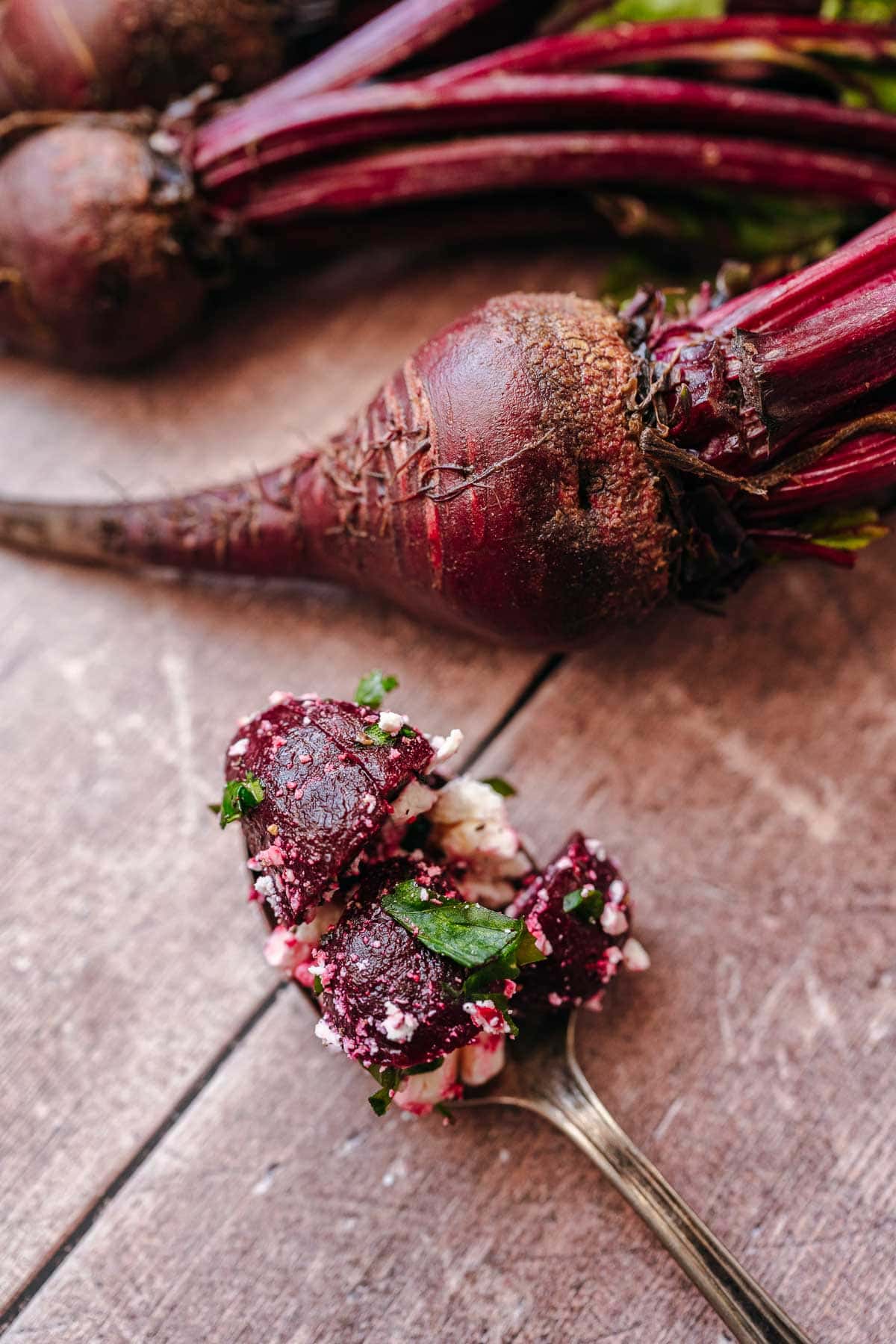 A silver spoon holding beets and feta cheese rests on a wood table.