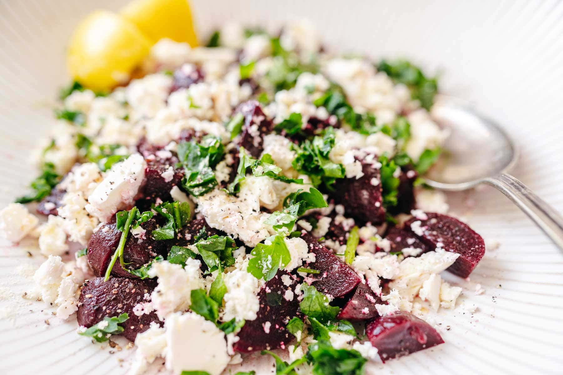 A large white ceramic bowl with beets feta cheese and parsley.