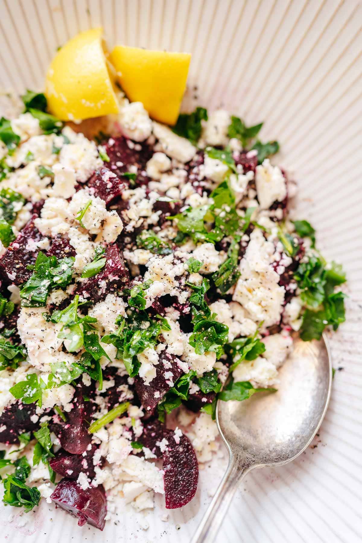 Close shot of a large white ceramic bowl with cubed beets, crumbled feta cheese and fresh green herbs.