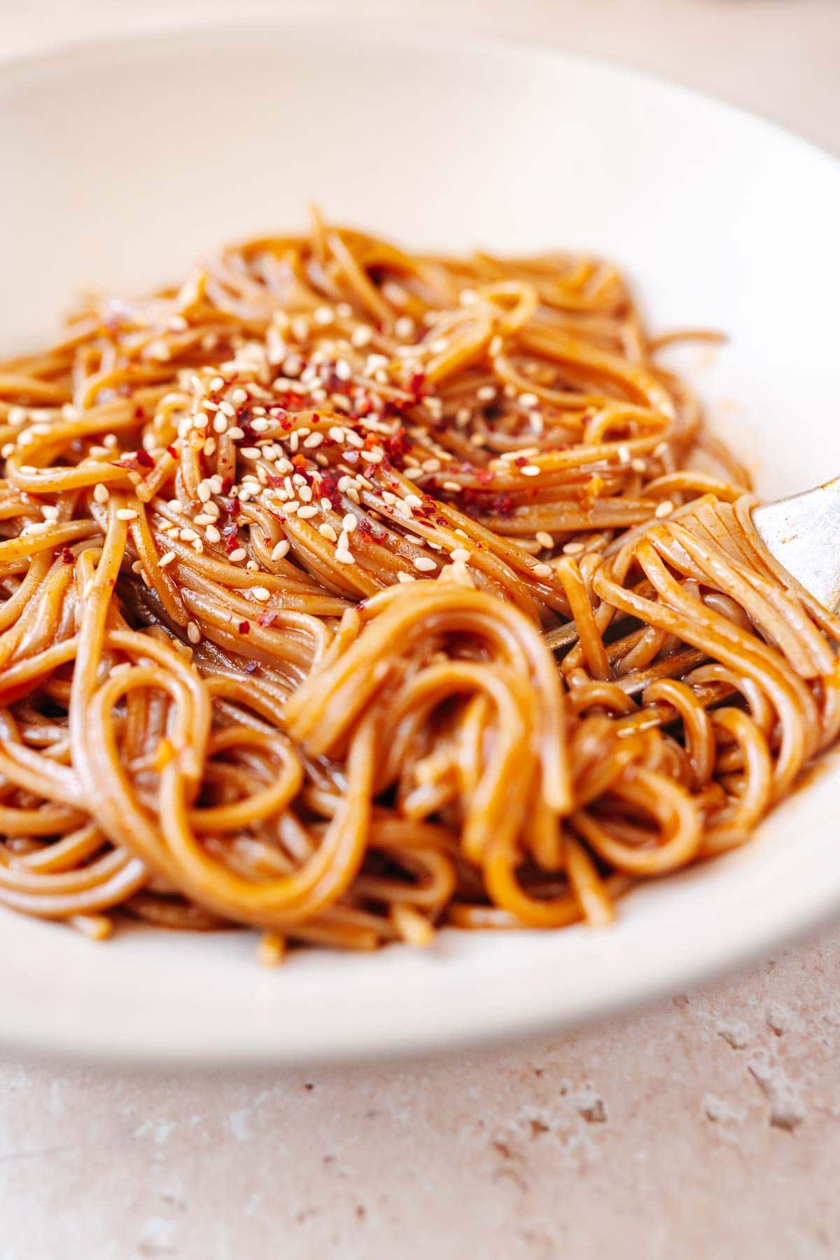 Side shot of a large bowl noodles coated in red sauce and garnished with sesame seeds.