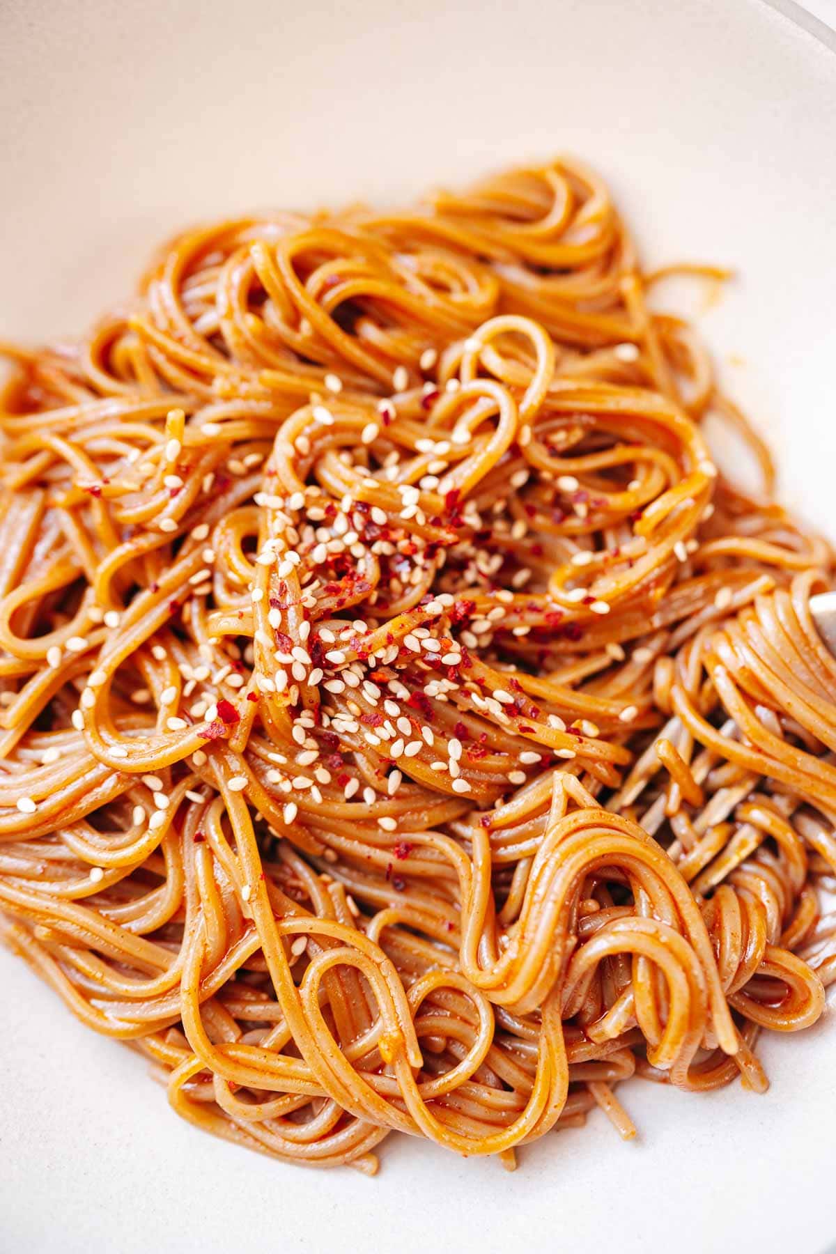 Noodles coated in a red creamy sauce and garnished with seeds and chile flakes.
