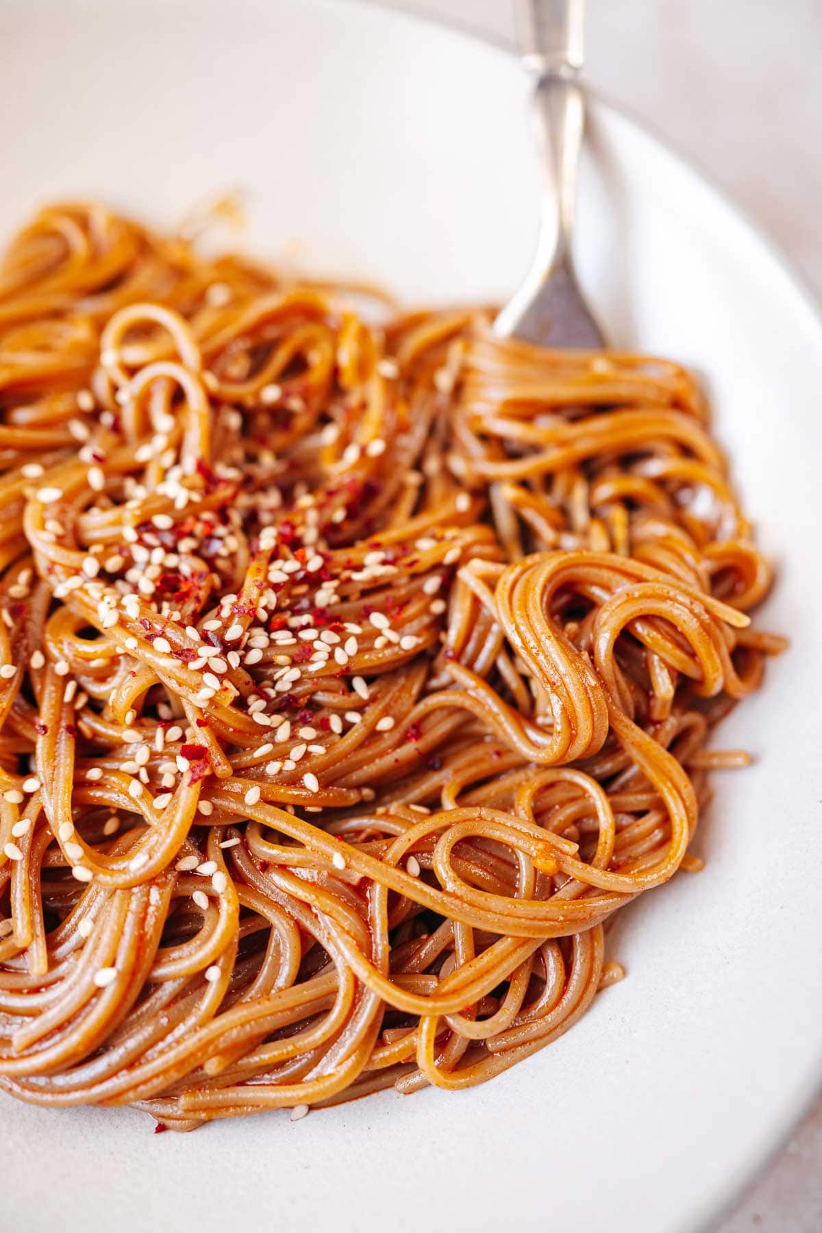 Close shot of creamy red noodles resting in a bowl with a silver fork.