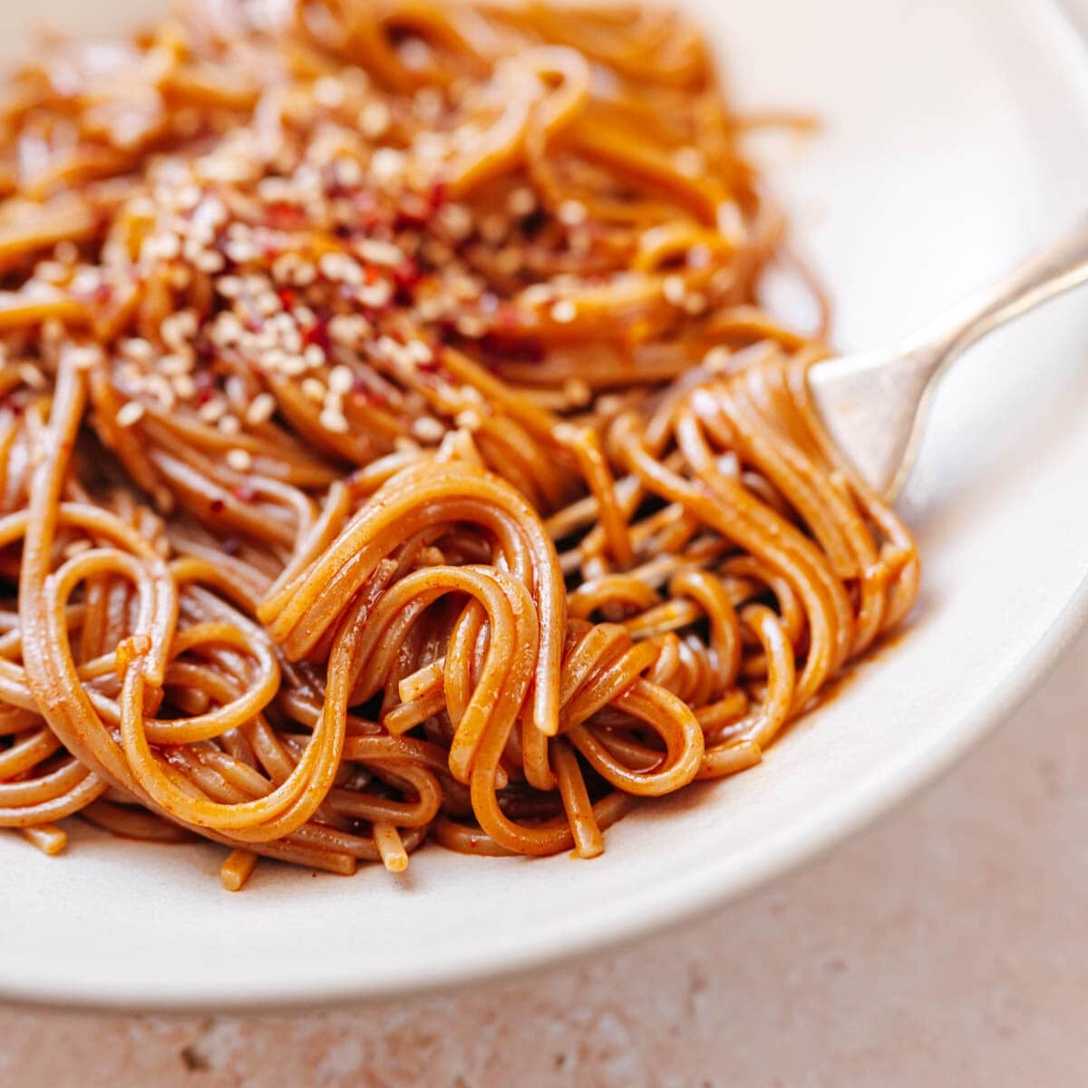 Close shot of red noodles wrapped around a silver fork resting in a white bowl.