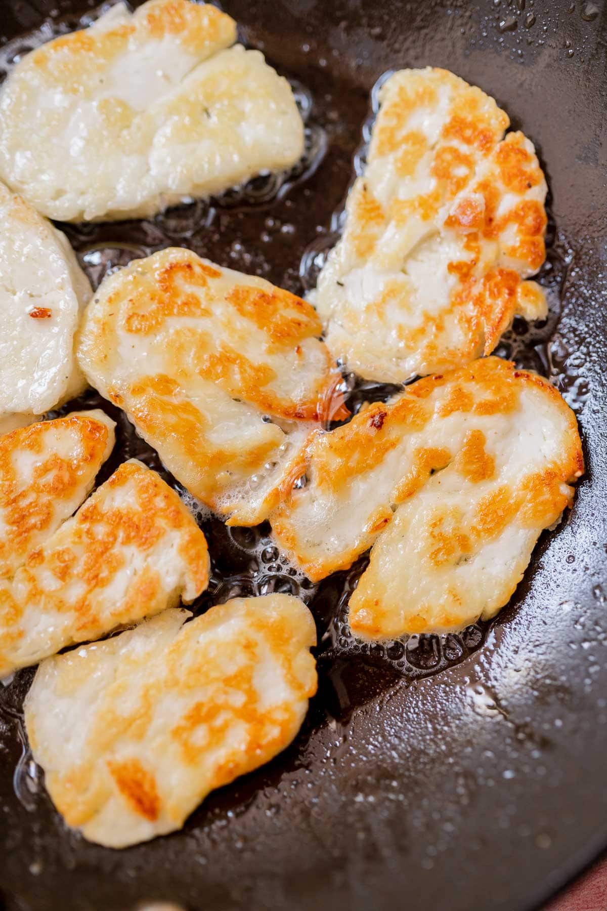 Crispy golden halloumi cheese slices resting in a black skillet.