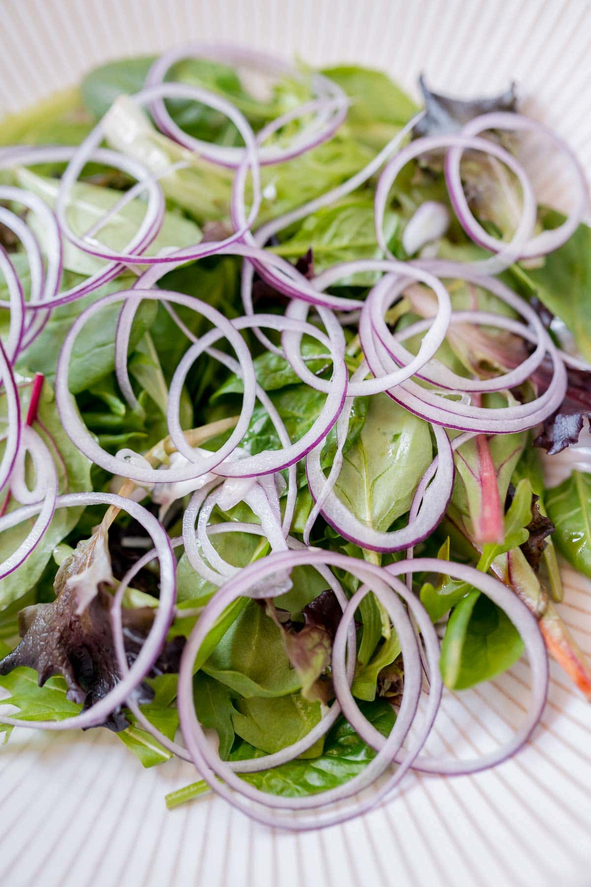 A large white bowl filled with salad greens and red onion slices.