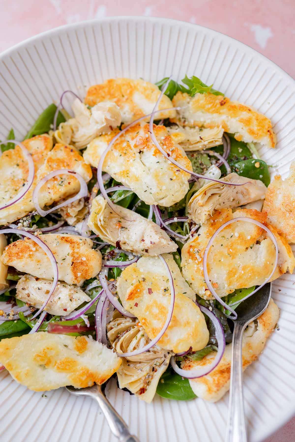 Silver silverware juts out of a large salad bowl filled with halloumi salad ingredients.